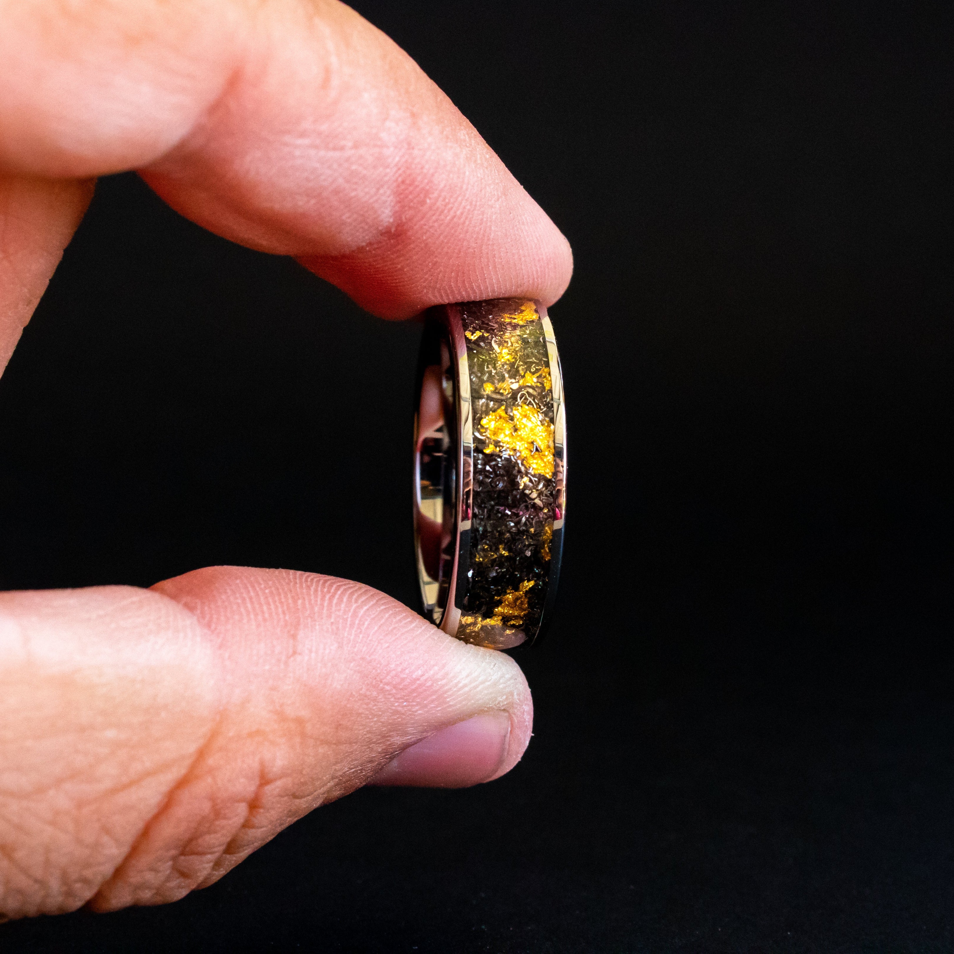 Shot of the 24K Cosmic Gold ring showing authentic Campo del Cielo meteorite shavings and real gold metal flake catching light on wide channel tungsten band