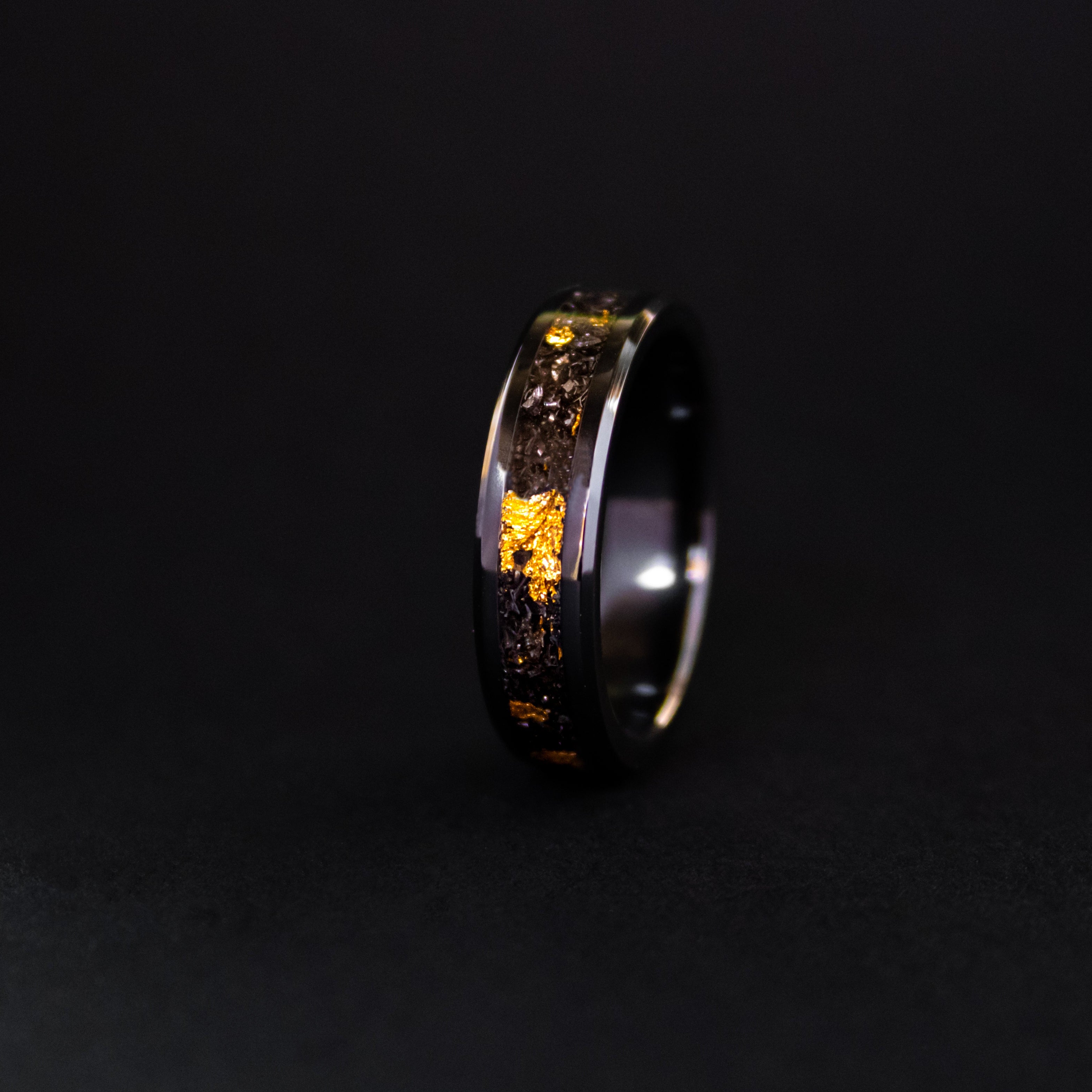 Detail shot of the 24K Cosmic Ceramic ring showing authentic Campo del Cielo meteorite shavings and real gold metal flake catching light on beveled black ceramic band