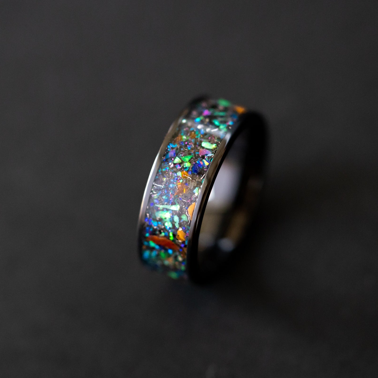 Detail shot of the Apex Predator Ceramic ring showing T-Rex and Velociraptor bone fragments and meteorite shavings catching light through blue and green galaxy opal inlay
