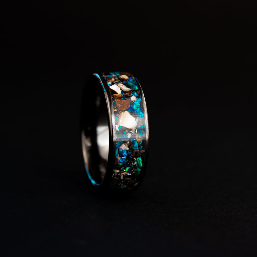 Detail shot of the Blue Fossils ring showing Mosasaur bone, Dinosaur Gembone, and meteorite fragments catching light through blue opal inlay on wide channel ceramic band