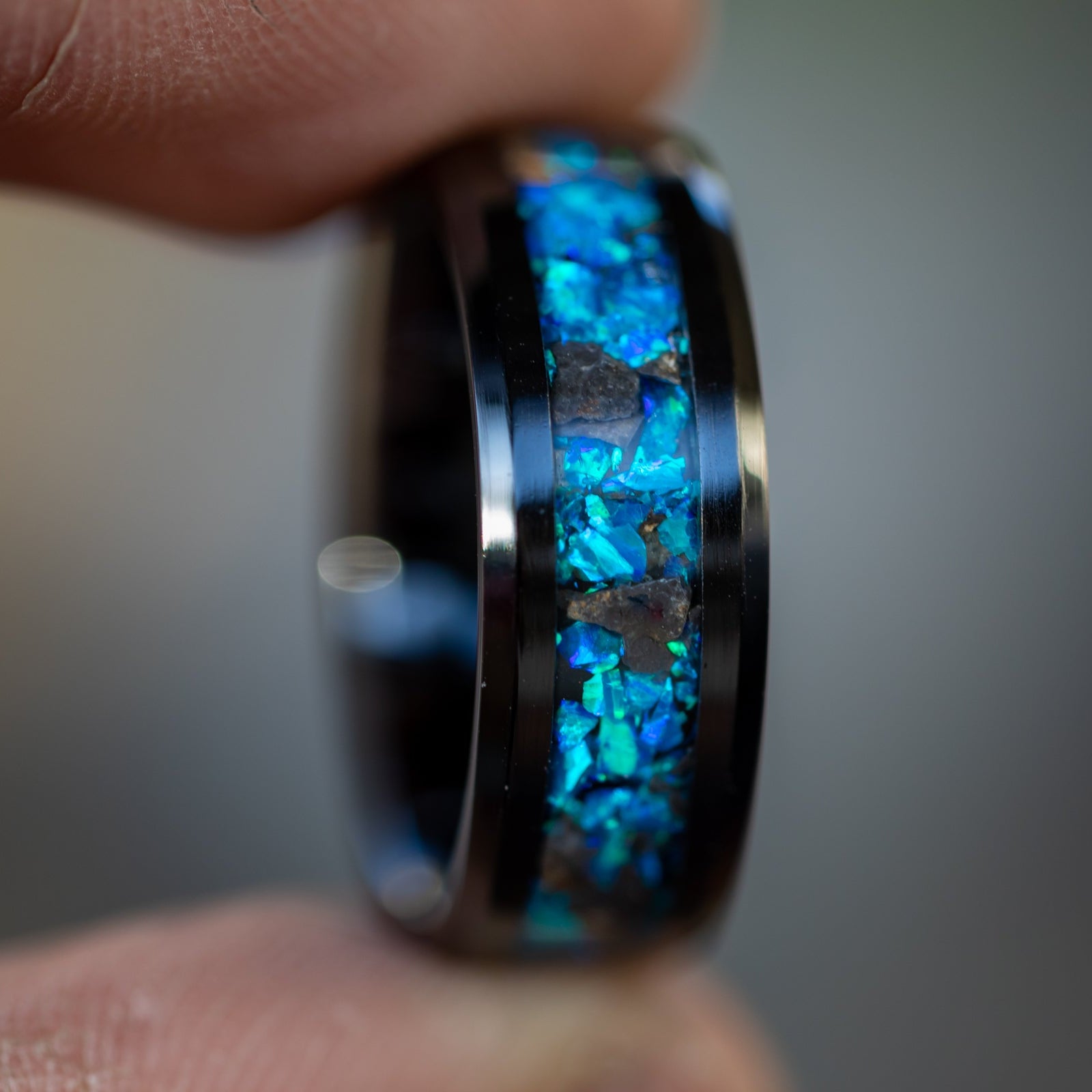Blue Moon ring showing authentic lunar meteorite fragments catching light through deep blue opal inlay on black ceramic band