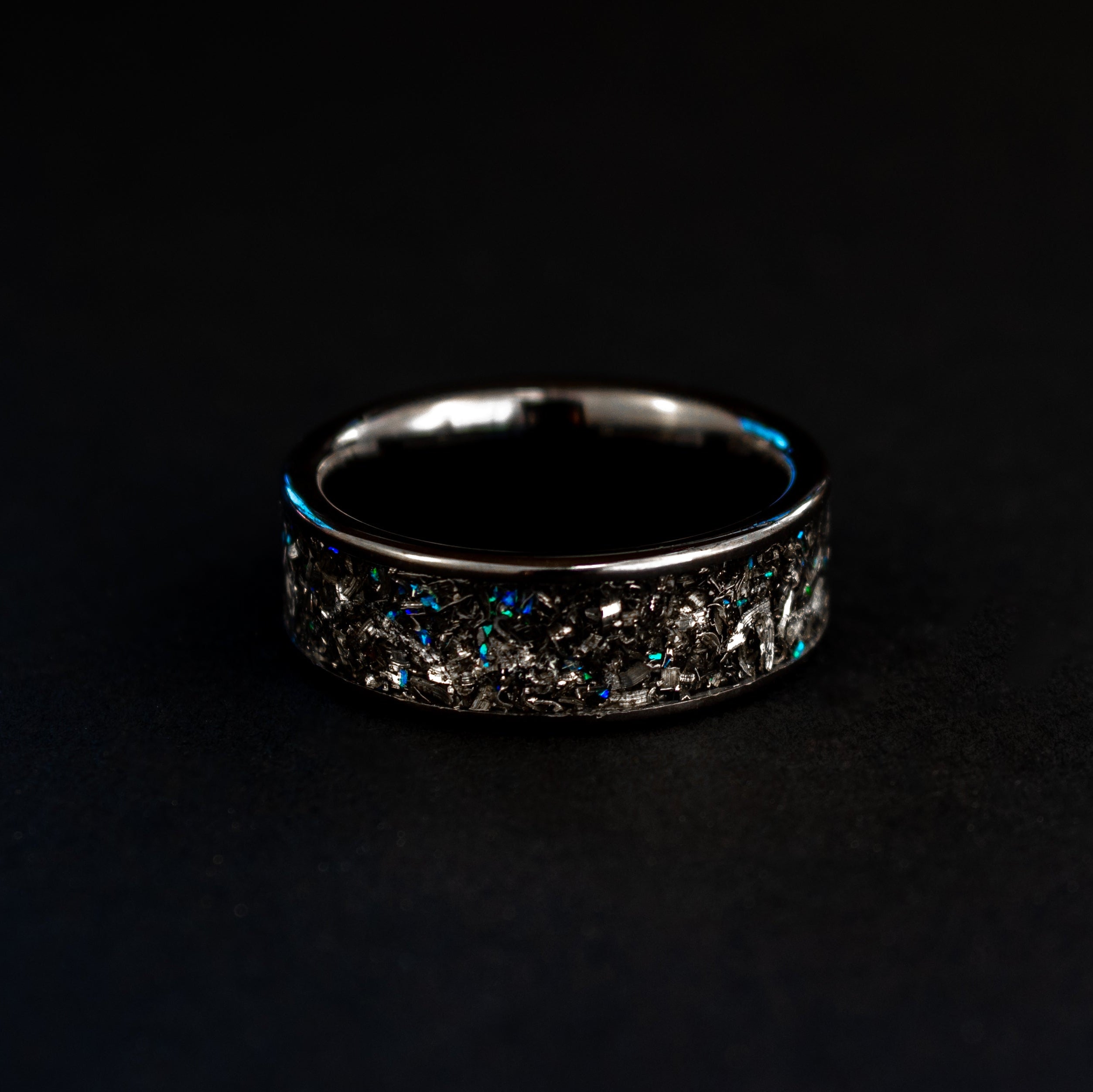 Detail shot of the Blue Spark Ceramic ring showing authentic Campo del Cielo meteorite shavings and subtle blue opal accents catching light on wide channel black ceramic band