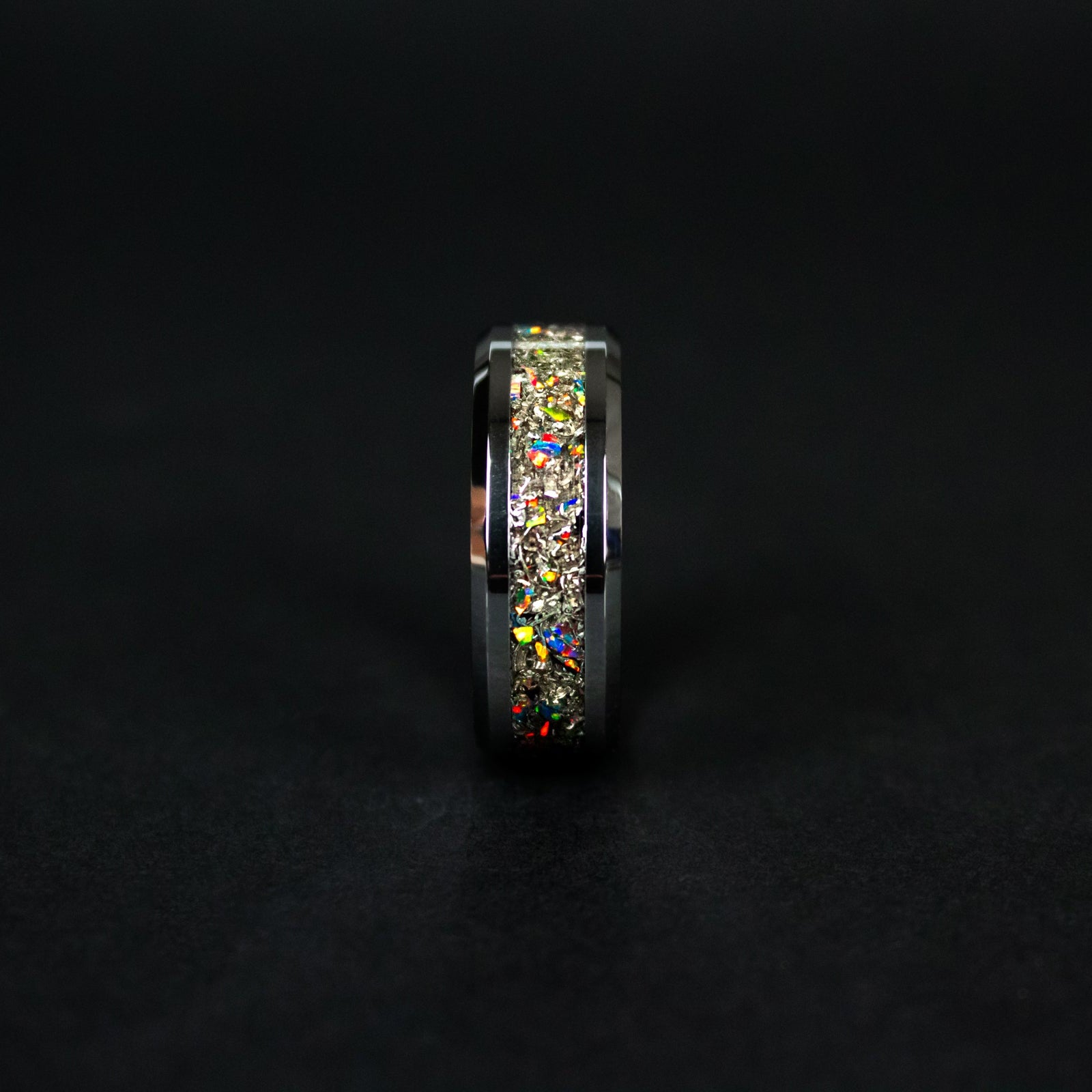 Close up of genuine Campo del Cielo meteorite shavings with scattered black fire opal accents flashing hidden color on beveled tungsten ring