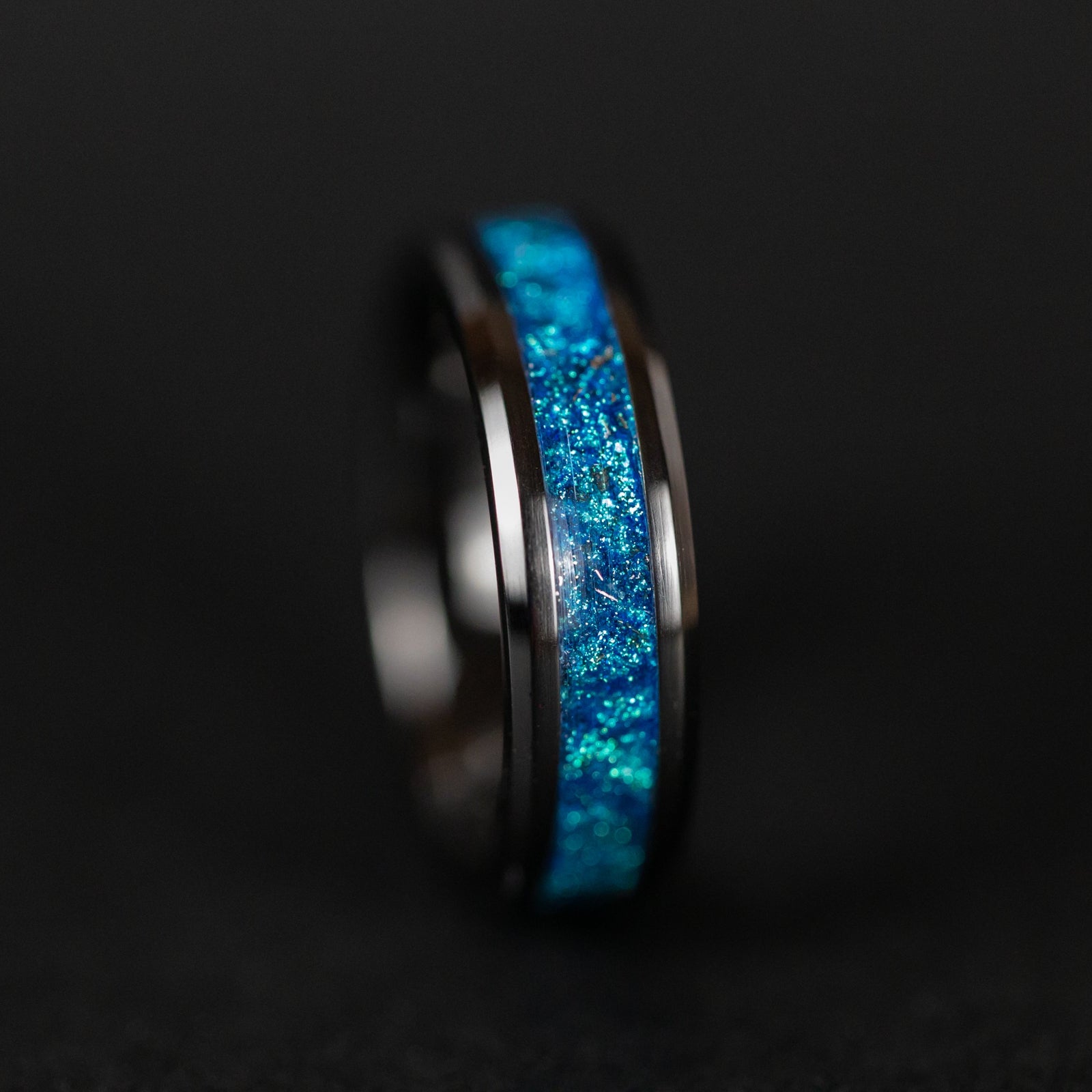Close up of genuine Campo del Cielo meteorite shavings suspended in rich blue glitter pigment inlay on beveled black ceramic ring