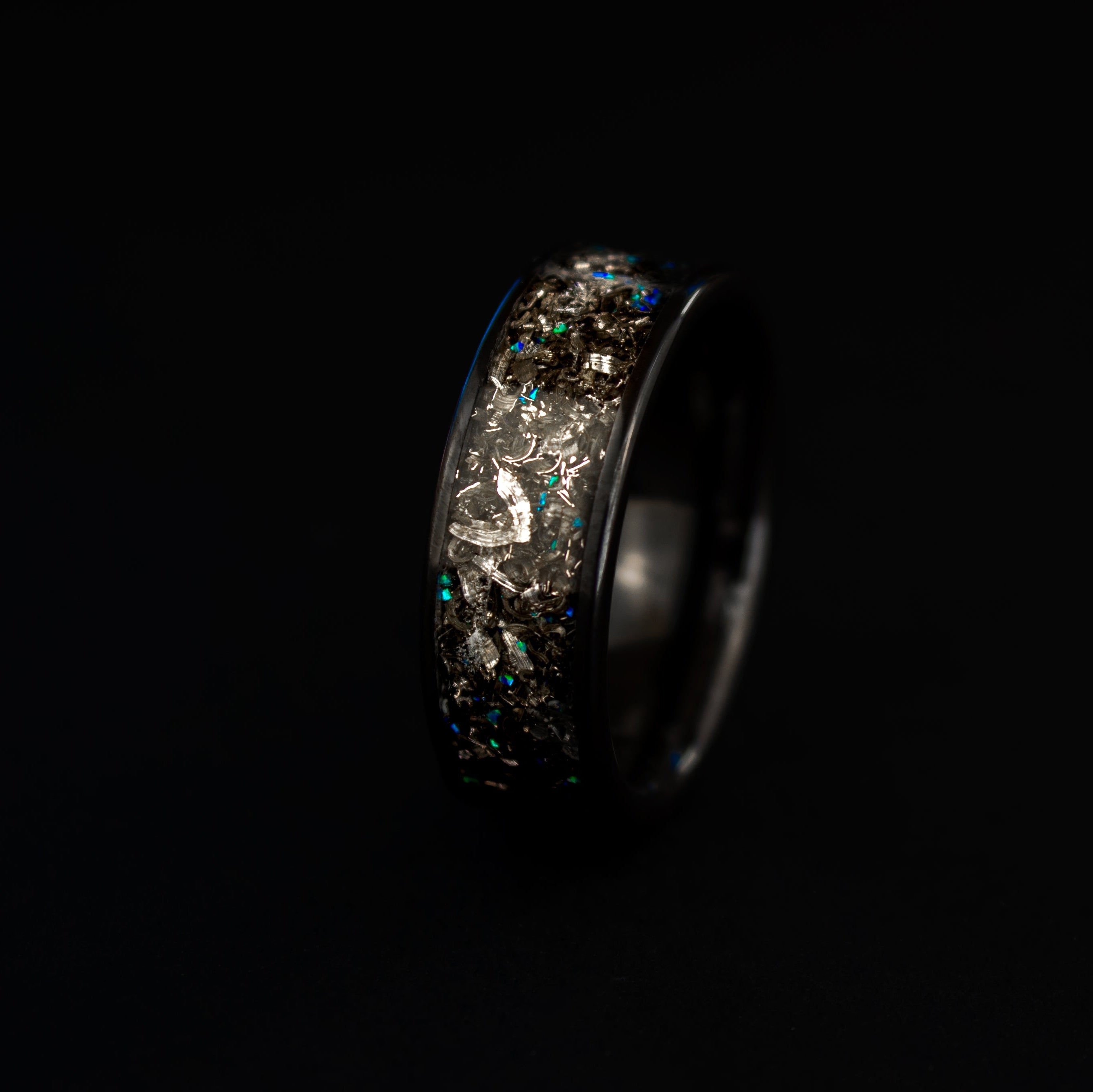 Close up of genuine Campo del Cielo meteorite shavings with scattered blue opal accents on wide channel black ceramic ring