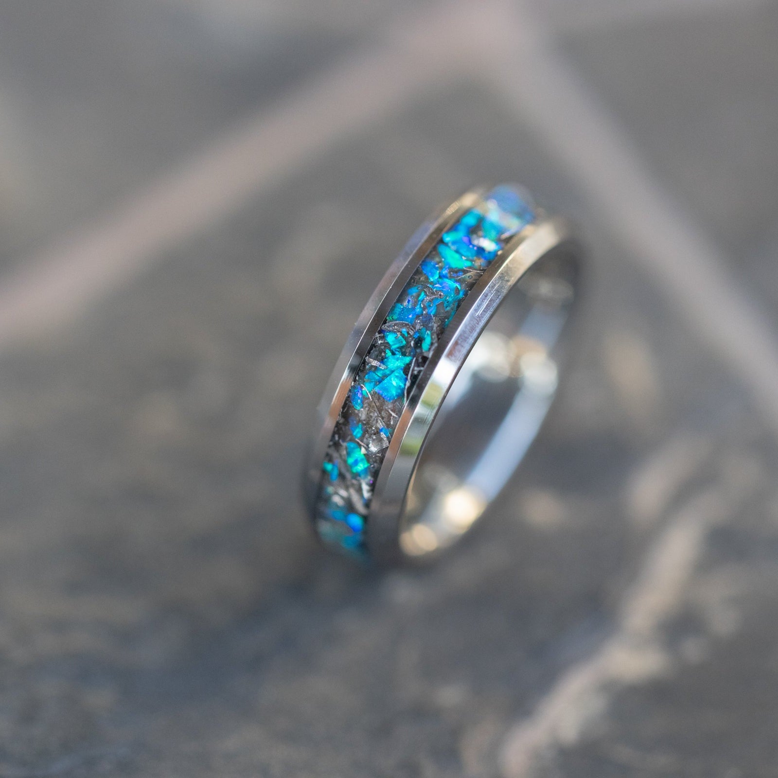 Close up of genuine Campo del Cielo meteorite shavings suspended in premium blue opal inlay on beveled tungsten ring
