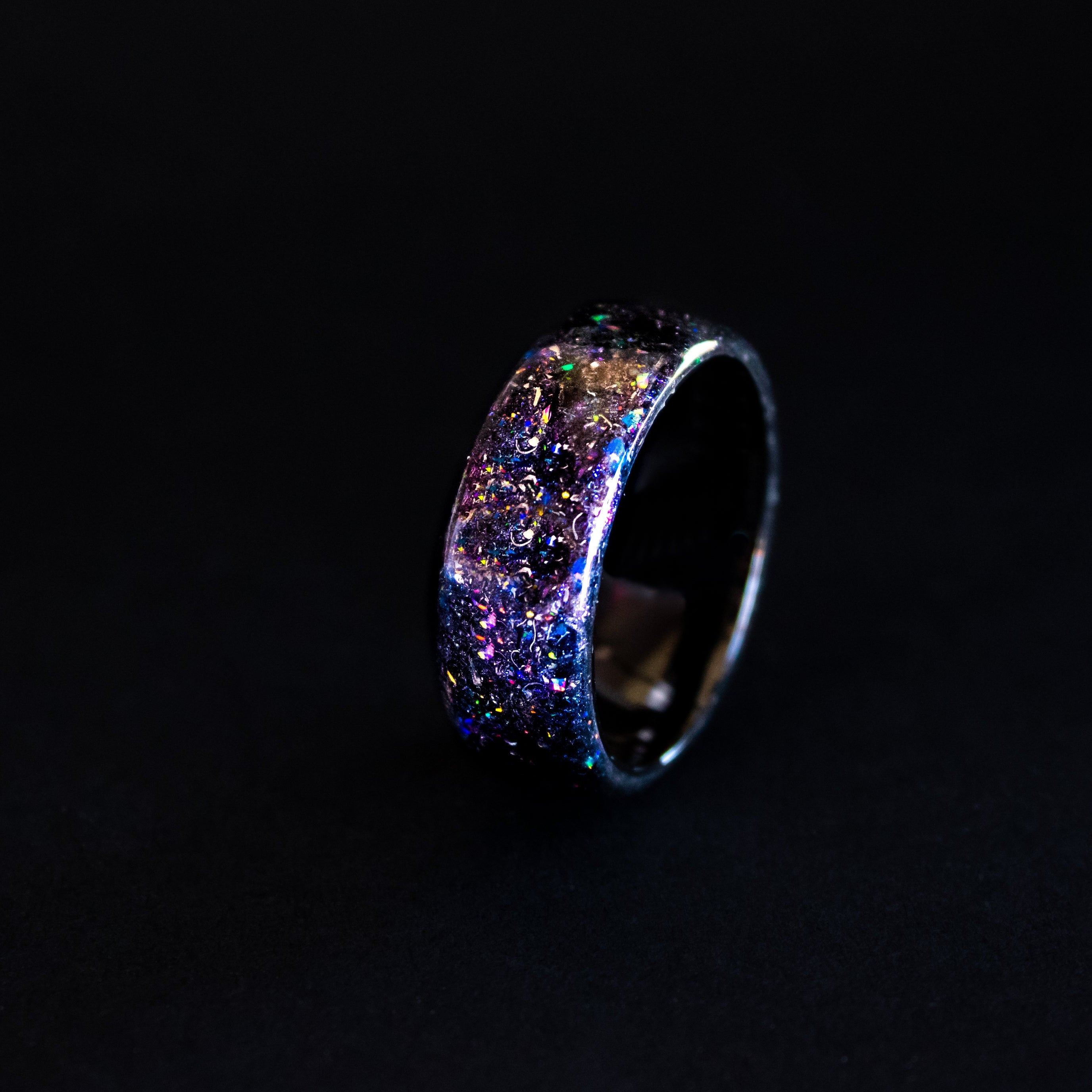 Close up of genuine Campo del Cielo meteorite shavings suspended in blue and purple opal galaxy pigment inlay on endless black ceramic ring