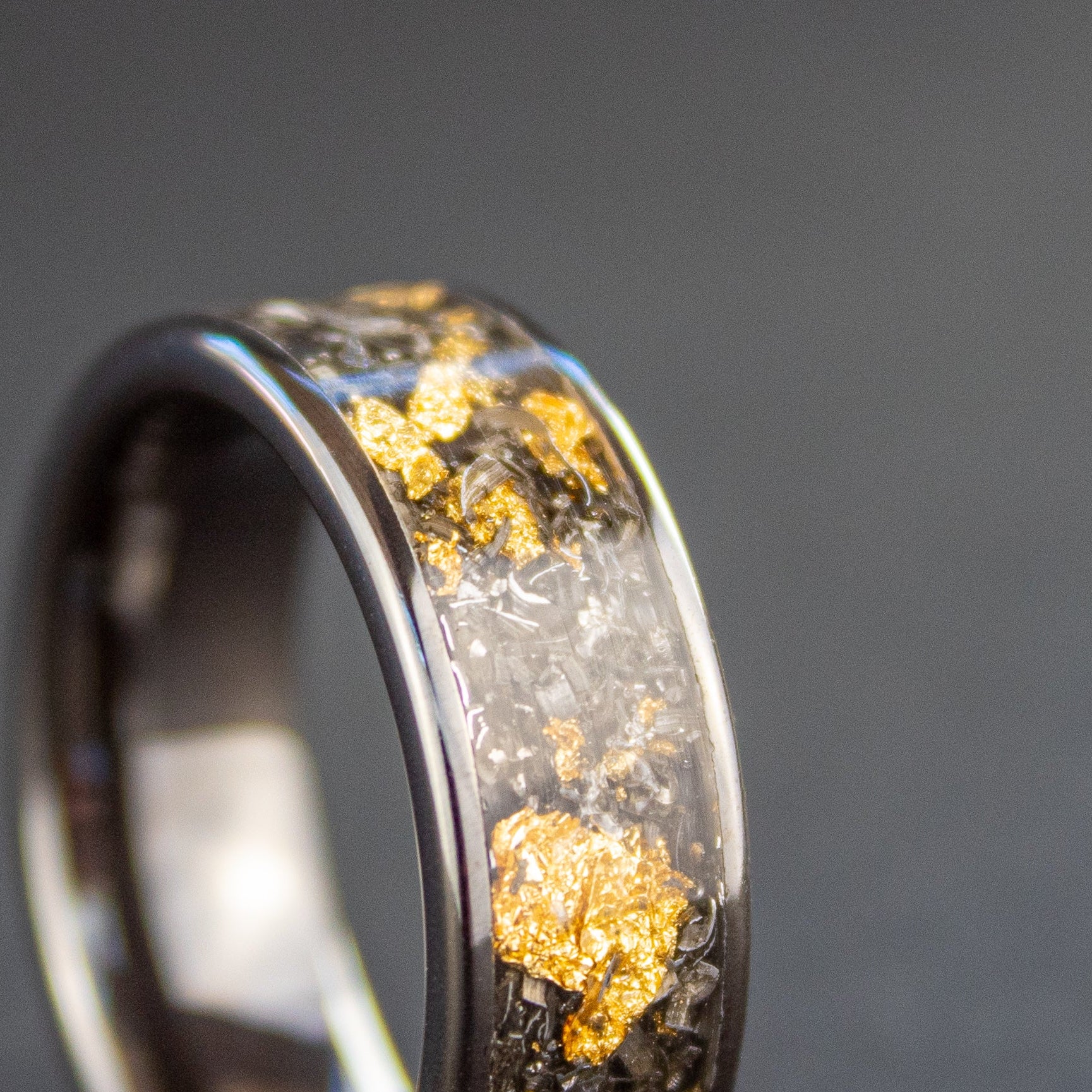 Close up of genuine Campo del Cielo meteorite shavings mixed with real gold metal flake inlay on wide channel black ceramic ring