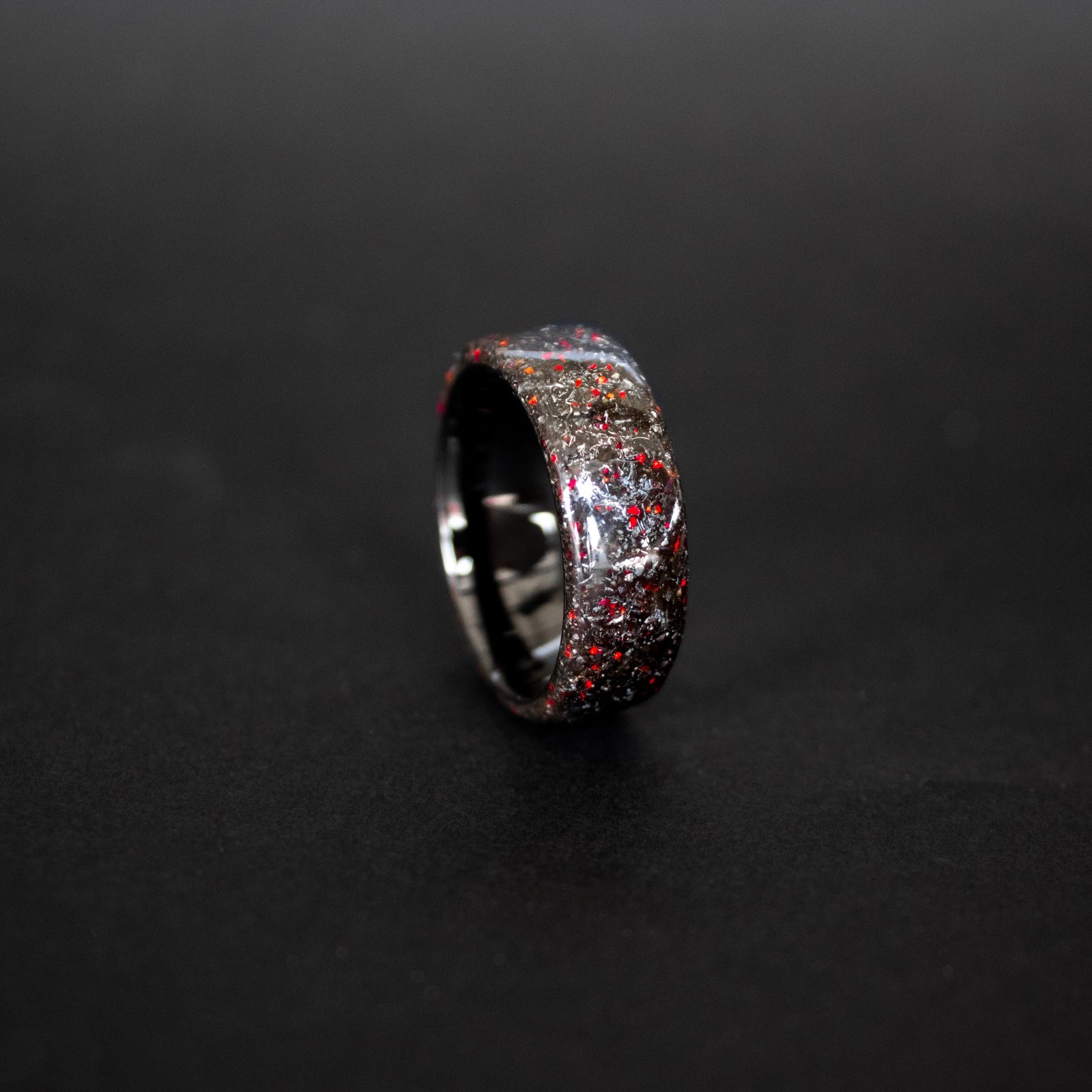Close up of genuine Campo del Cielo meteorite shavings with scattered red opal accents on endless black ceramic ring