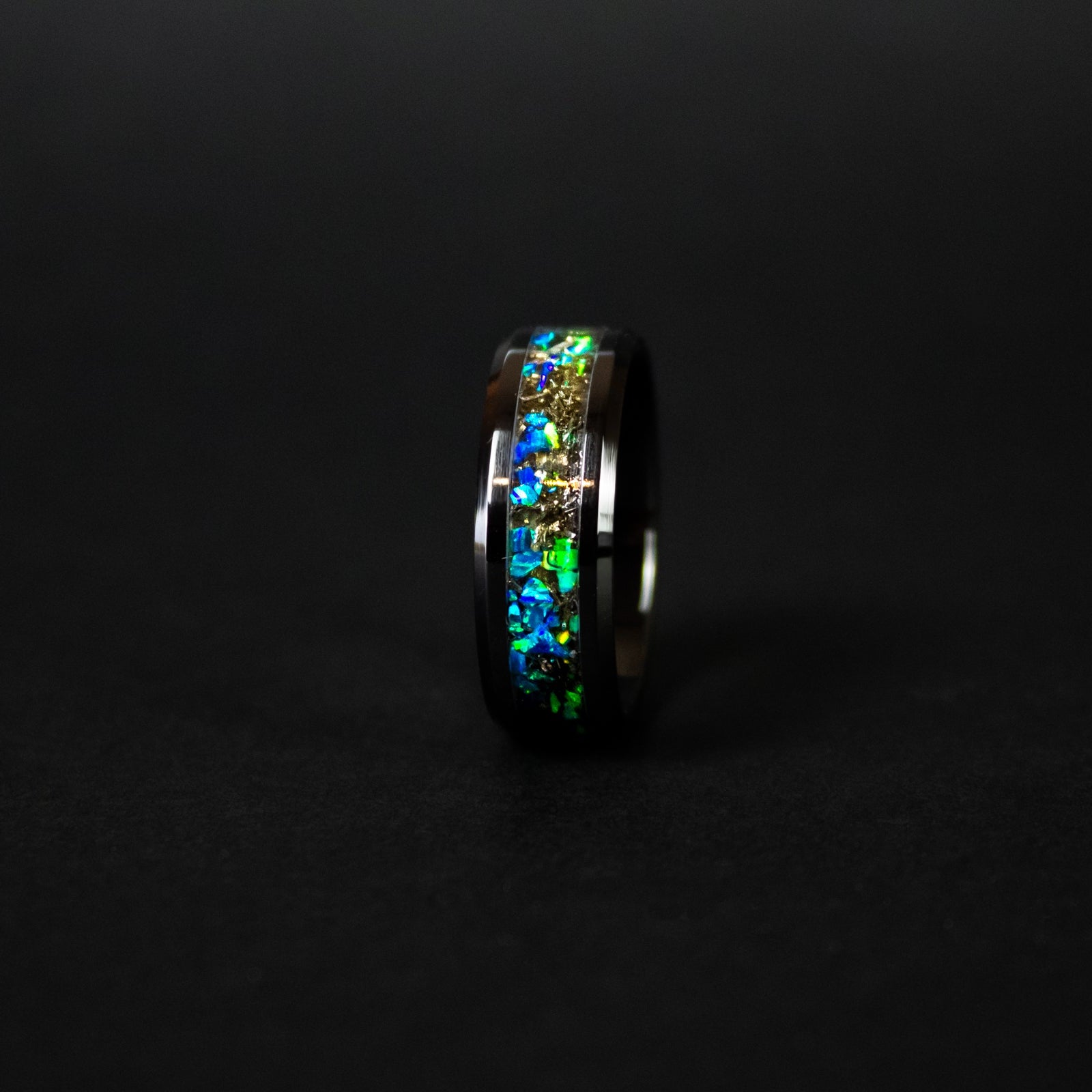 Close up of genuine Campo del Cielo meteorite shavings scattered across split blue and green opal inlay on beveled black ceramic ring