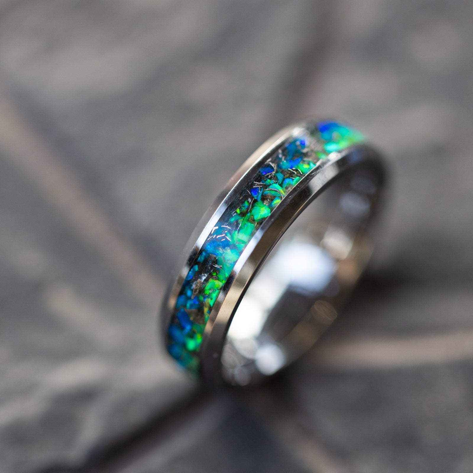 Close up of genuine Campo del Cielo meteorite shavings scattered across split blue and green opal inlay on beveled tungsten ring