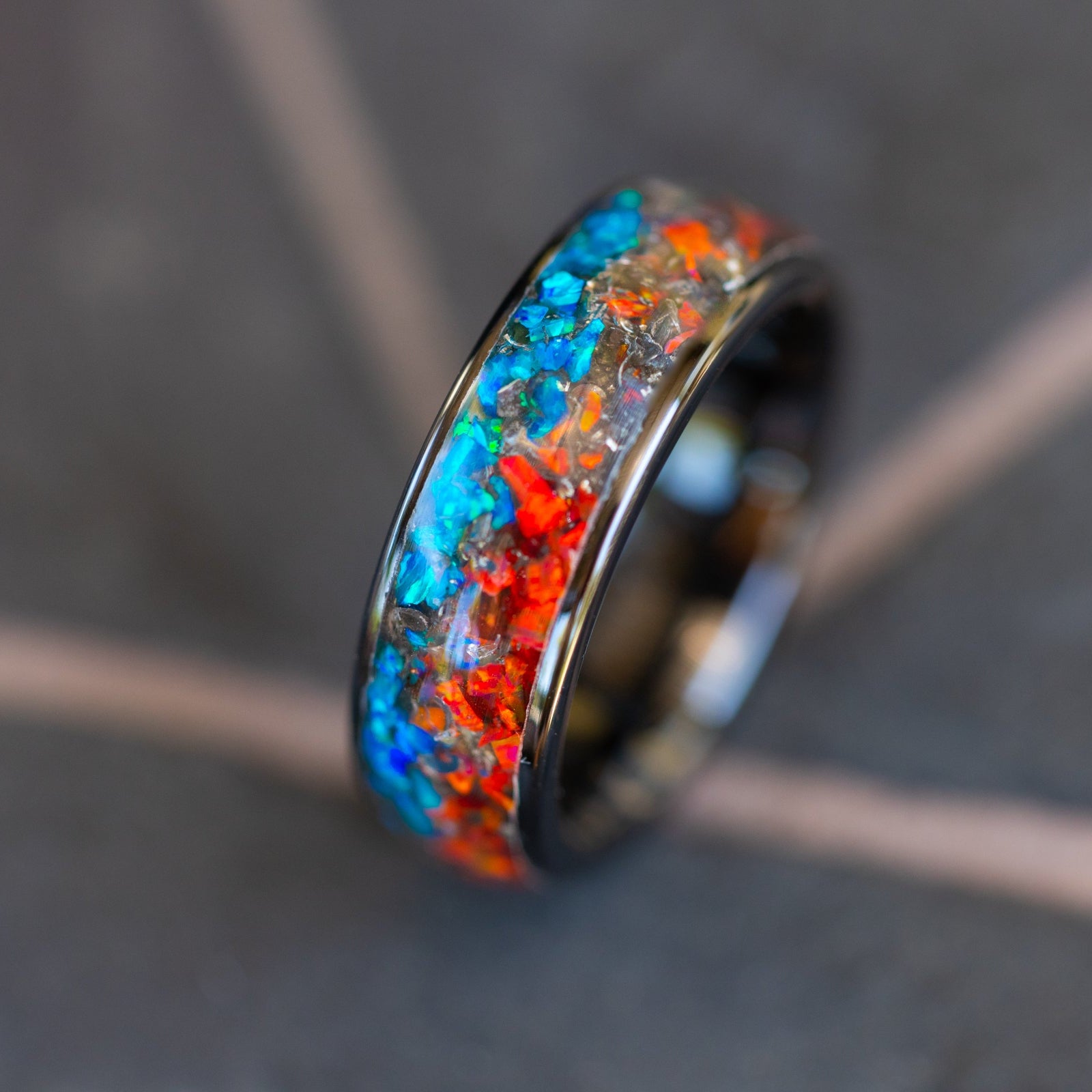 Close up of genuine Campo del Cielo meteorite shavings scattered across split red and blue opal inlay on wide channel ceramic ring