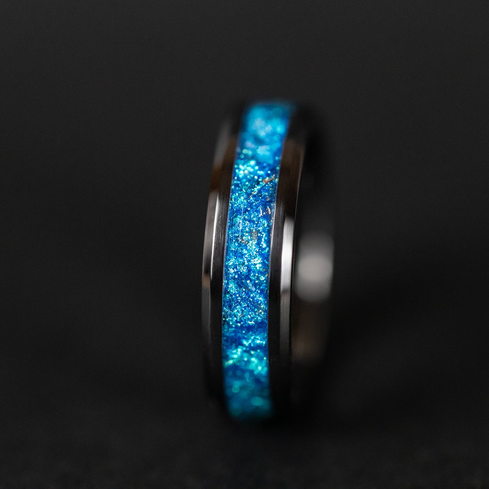 Detail shot of the Cobalt Orbit ring showing authentic Campo del Cielo meteorite shavings catching light through deep blue glitter pigment inlay on black ceramic band