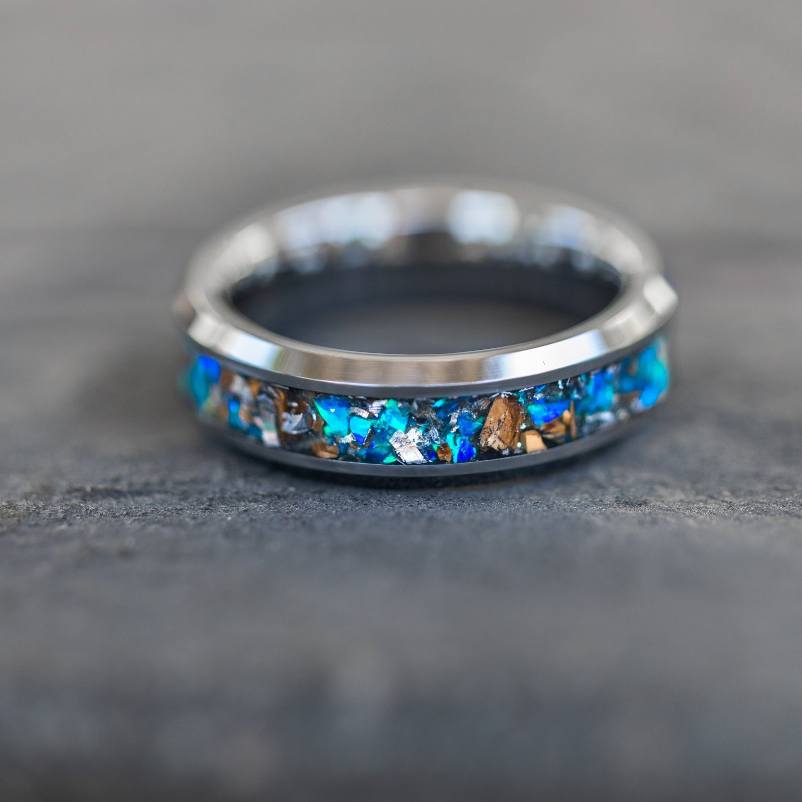 Detail shot of the Cobalt Rex Tungsten ring showing authentic Tyrannosaurus Rex bone fragments and meteorite shavings catching light through blue opal inlay