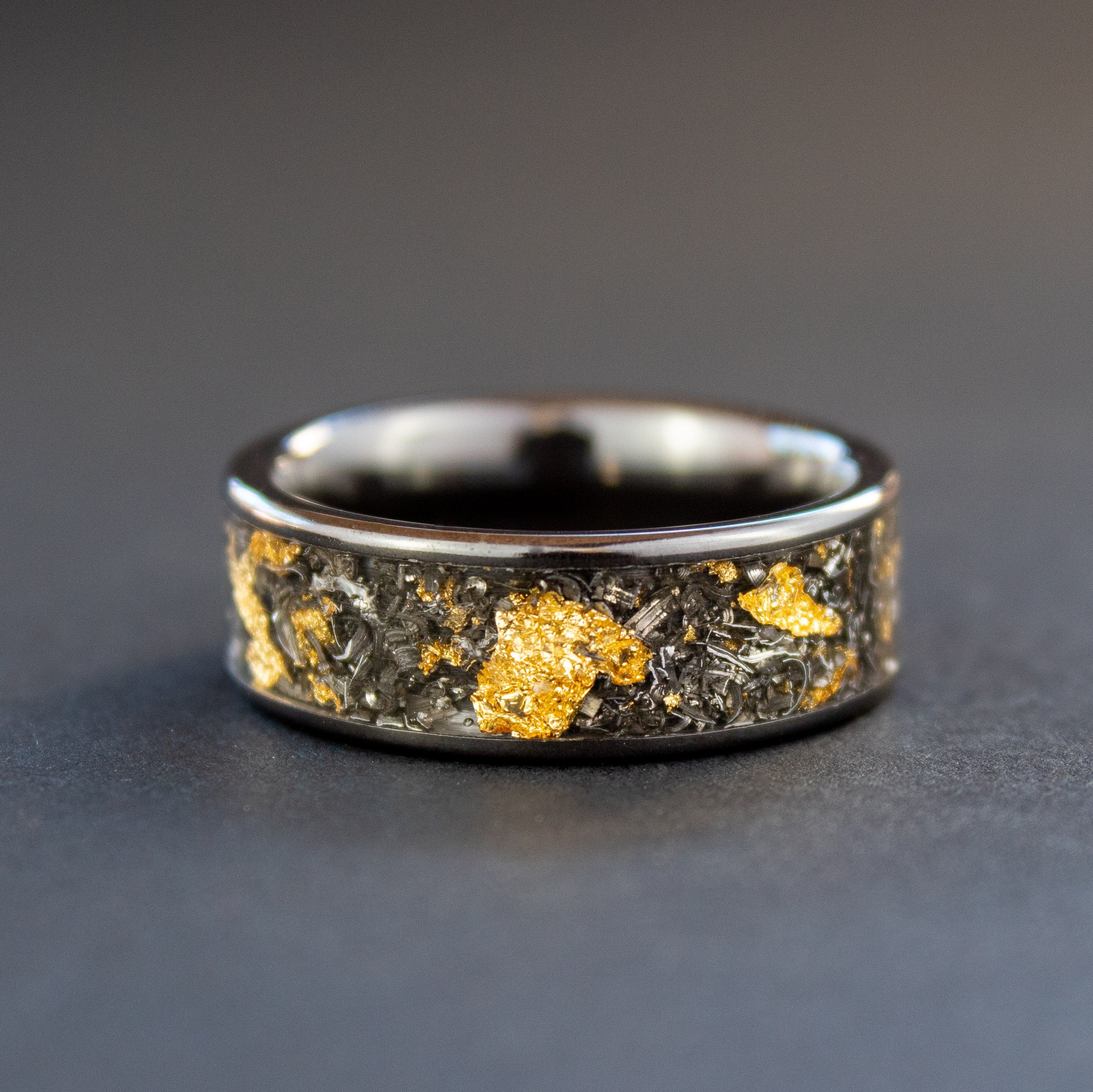 Detail shot of the Cosmic Gold Meteorite ring showing authentic Campo del Cielo meteorite shavings and real gold metal flake catching light on wide channel black ceramic band