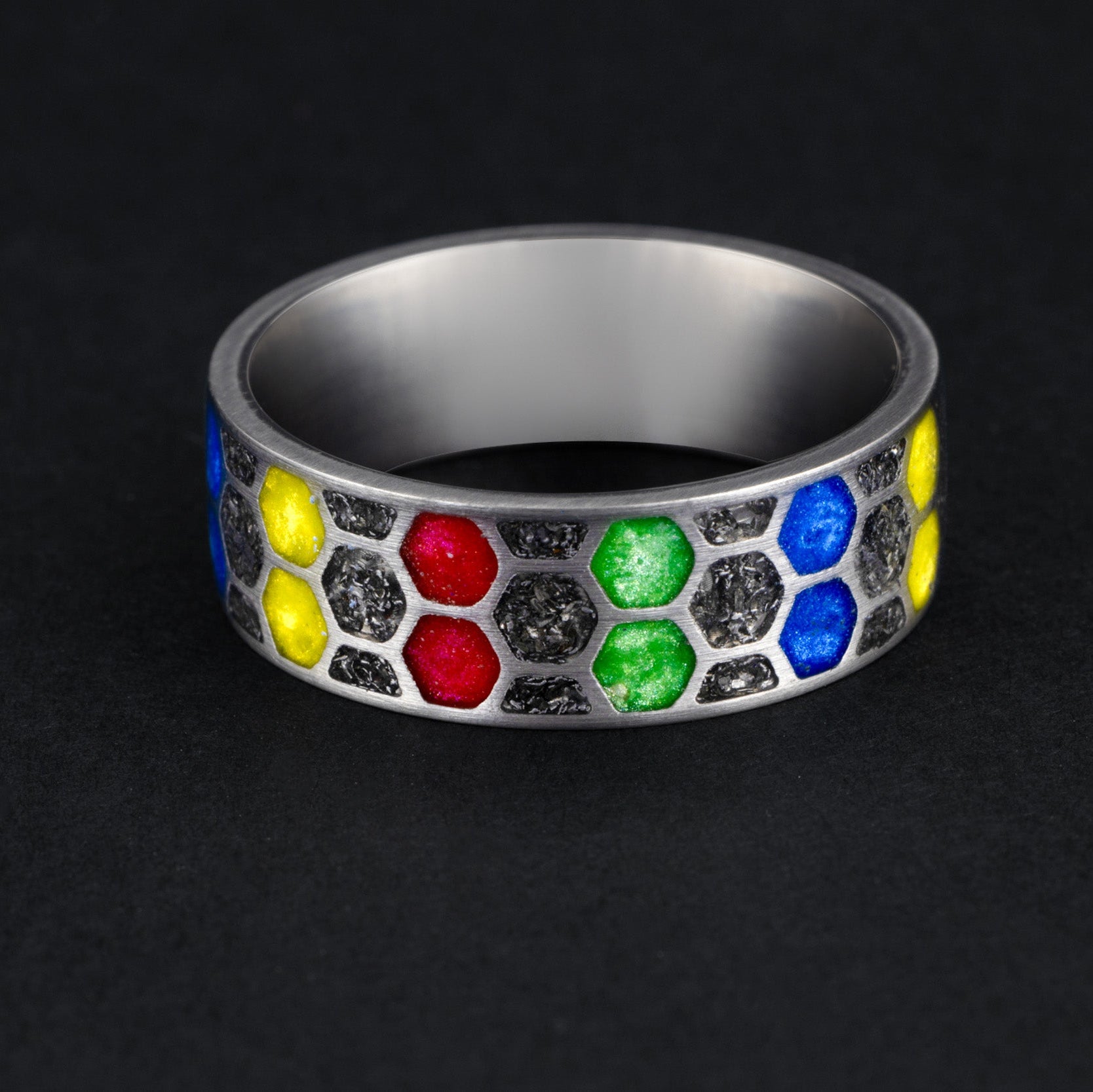 Detail shot of the Cosmic Infinity ring showing authentic Campo del Cielo meteorite dust and red blue yellow green resin filling individual honeycomb cells on titanium band