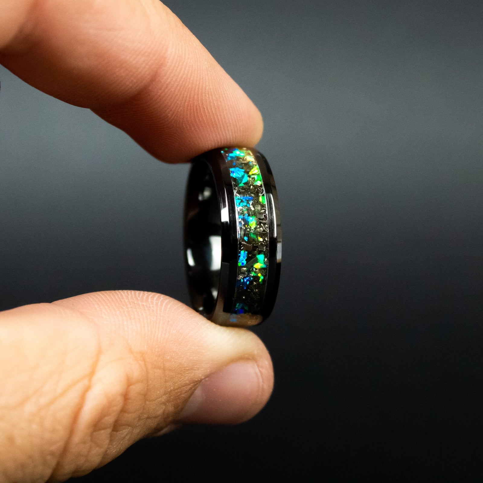 Detail shot of the Divided Seas ring showing authentic Campo del Cielo meteorite shavings bridging the transition between blue and green opal halves on black ceramic band