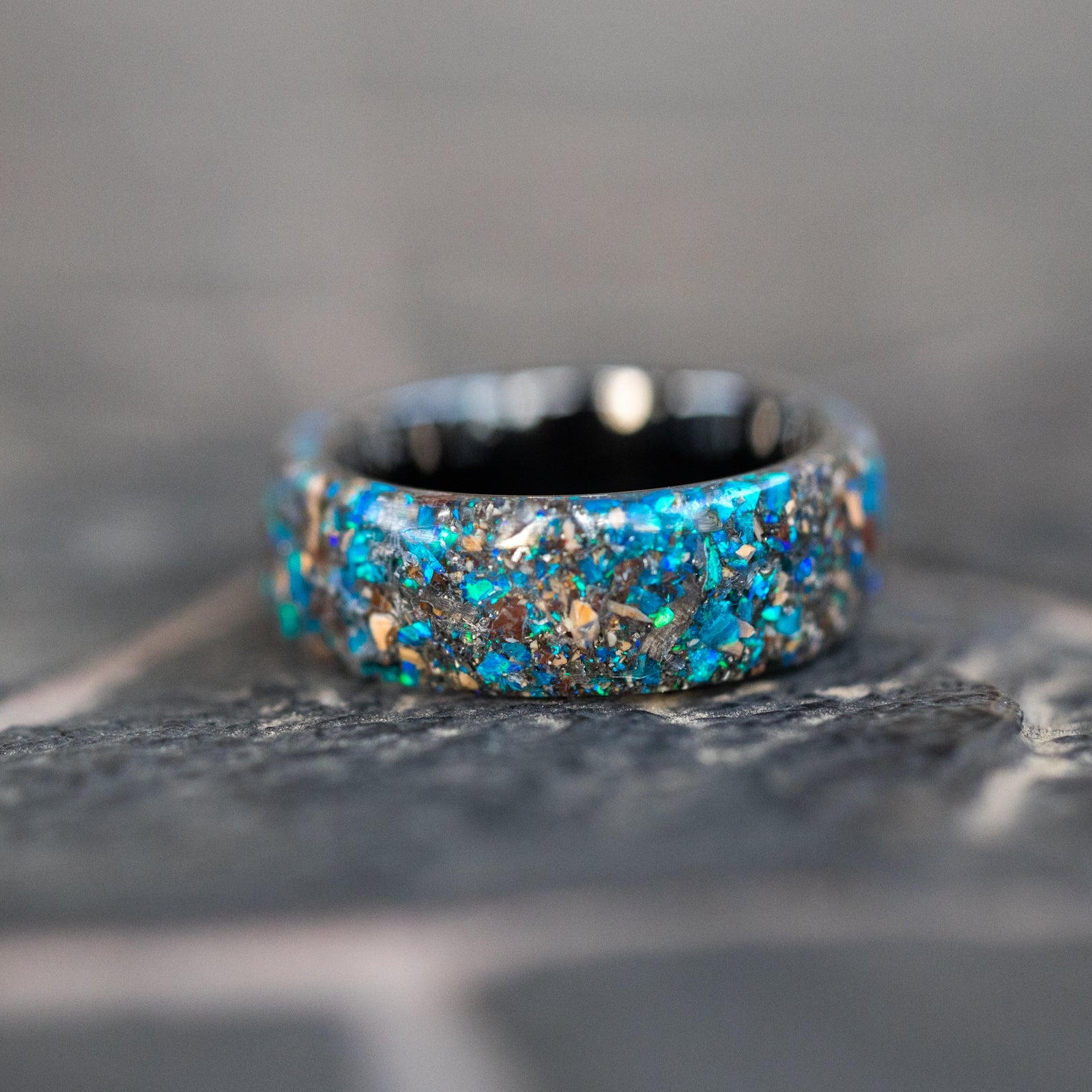 Detail shot of the Endless Deep Origin ring showing Mosasaur bone, Dinosaur Gembone, and meteorite fragments catching light through blue opal inlay