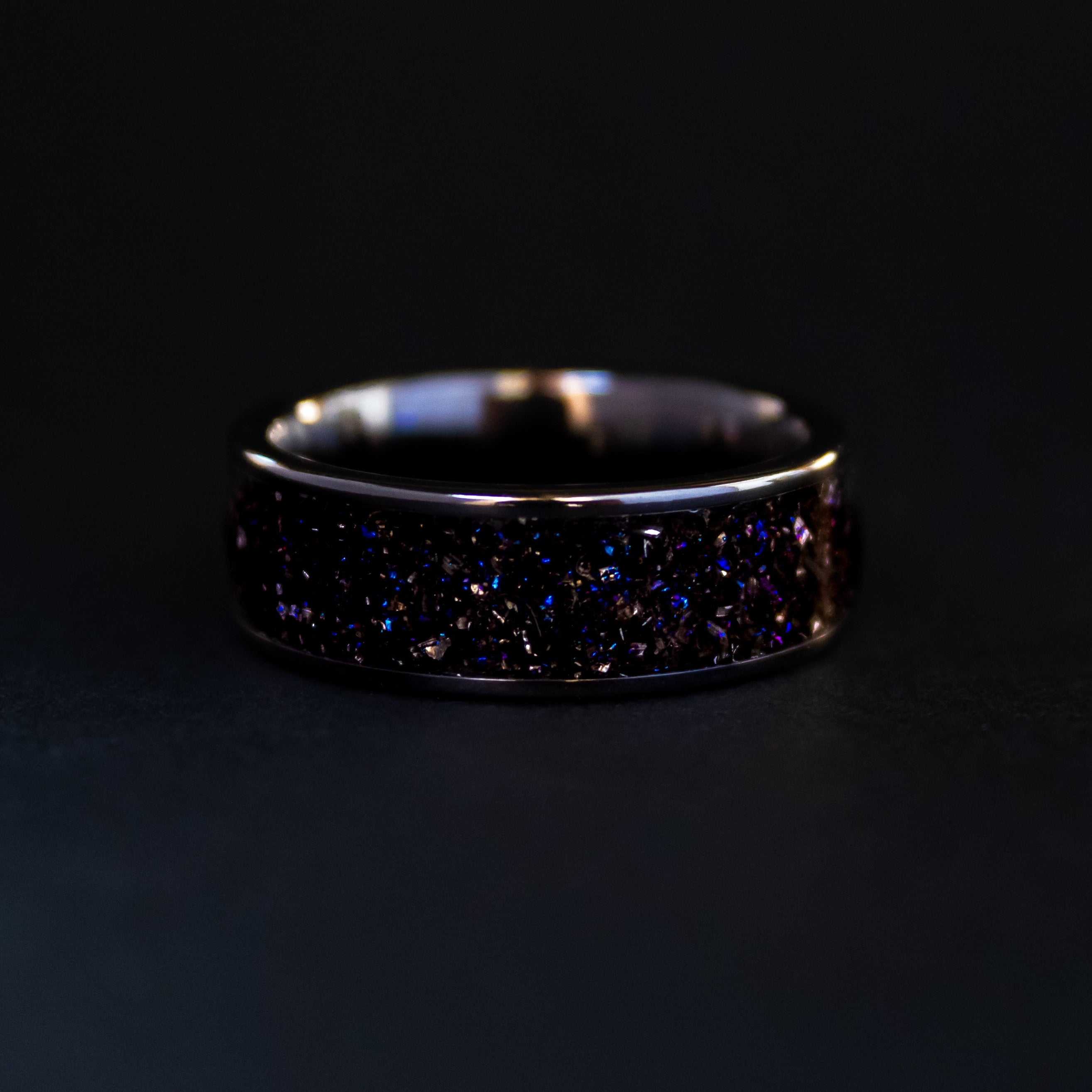 Detail shot of the Gibeon Galaxy ring showing authentic Gibeon meteorite shavings catching light through blue and purple galaxy glitter inlay on wide channel ceramic band