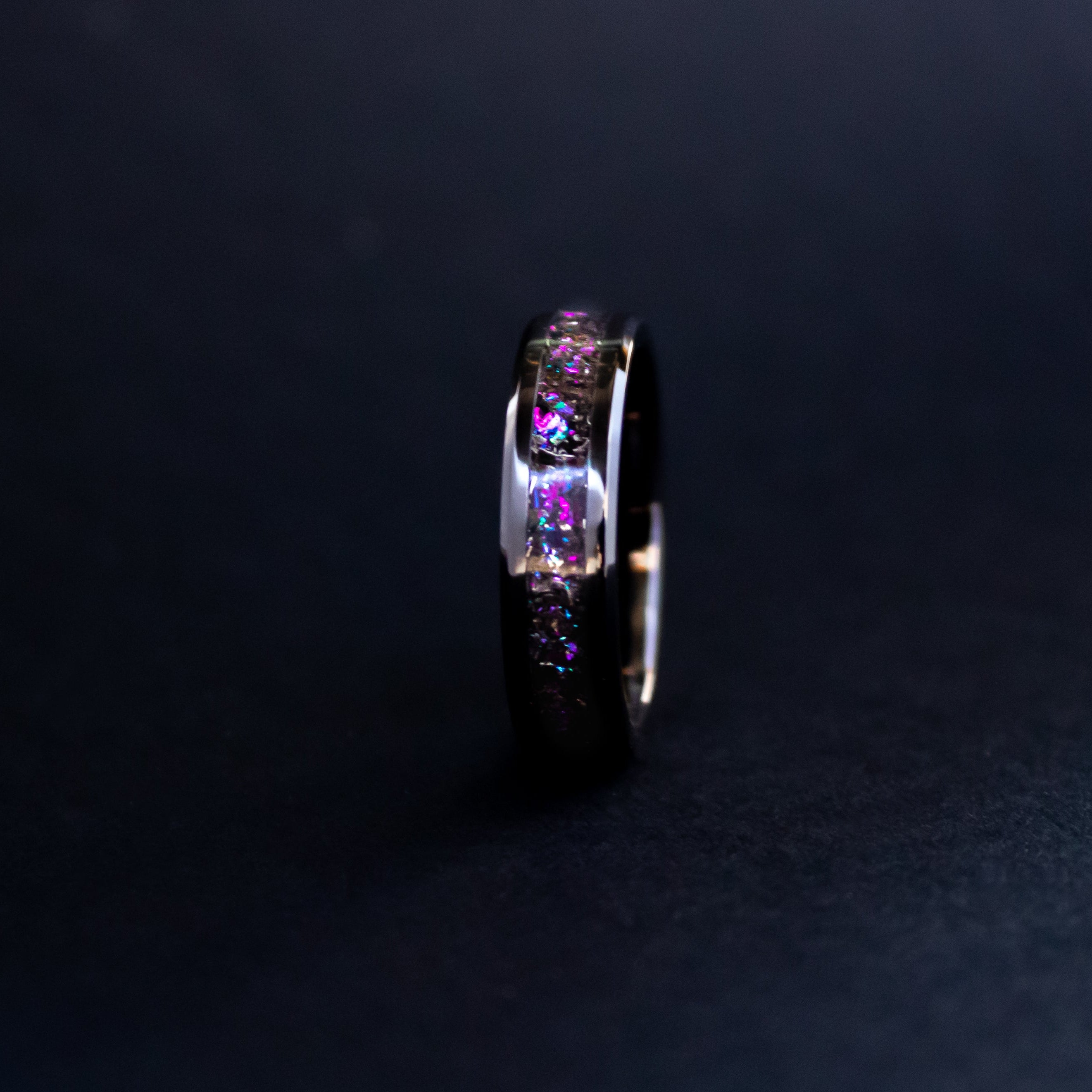 Detail shot of the Gibeon Galaxy Purple ring showing authentic Gibeon meteorite shavings catching light through pink and purple galaxy glitter inlay on beveled black ceramic band