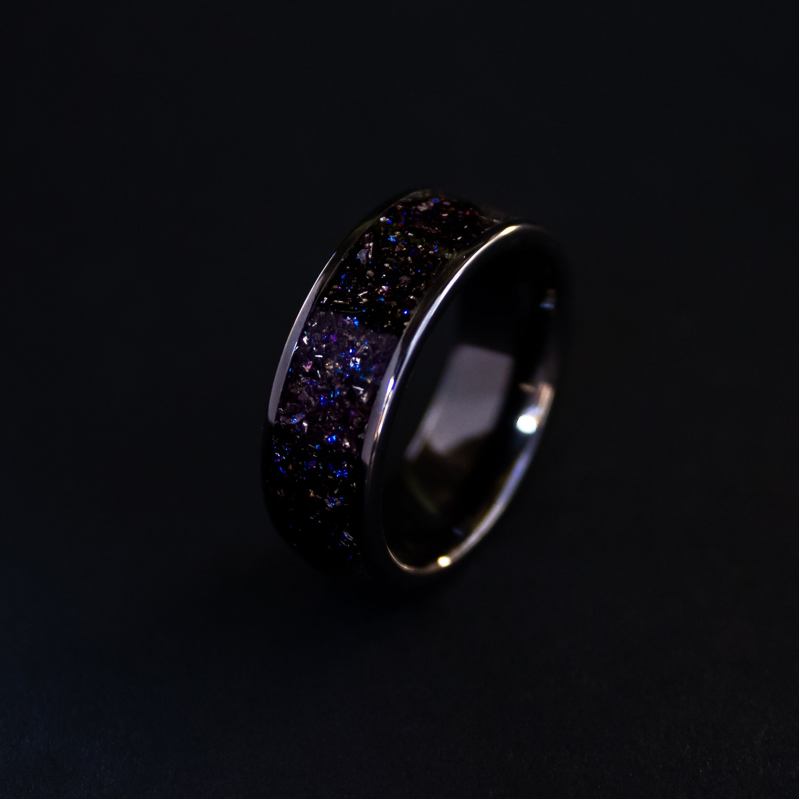 Close up of genuine Gibeon meteorite shavings suspended in blue and purple galaxy glitter inlay on wide channel black ceramic ring