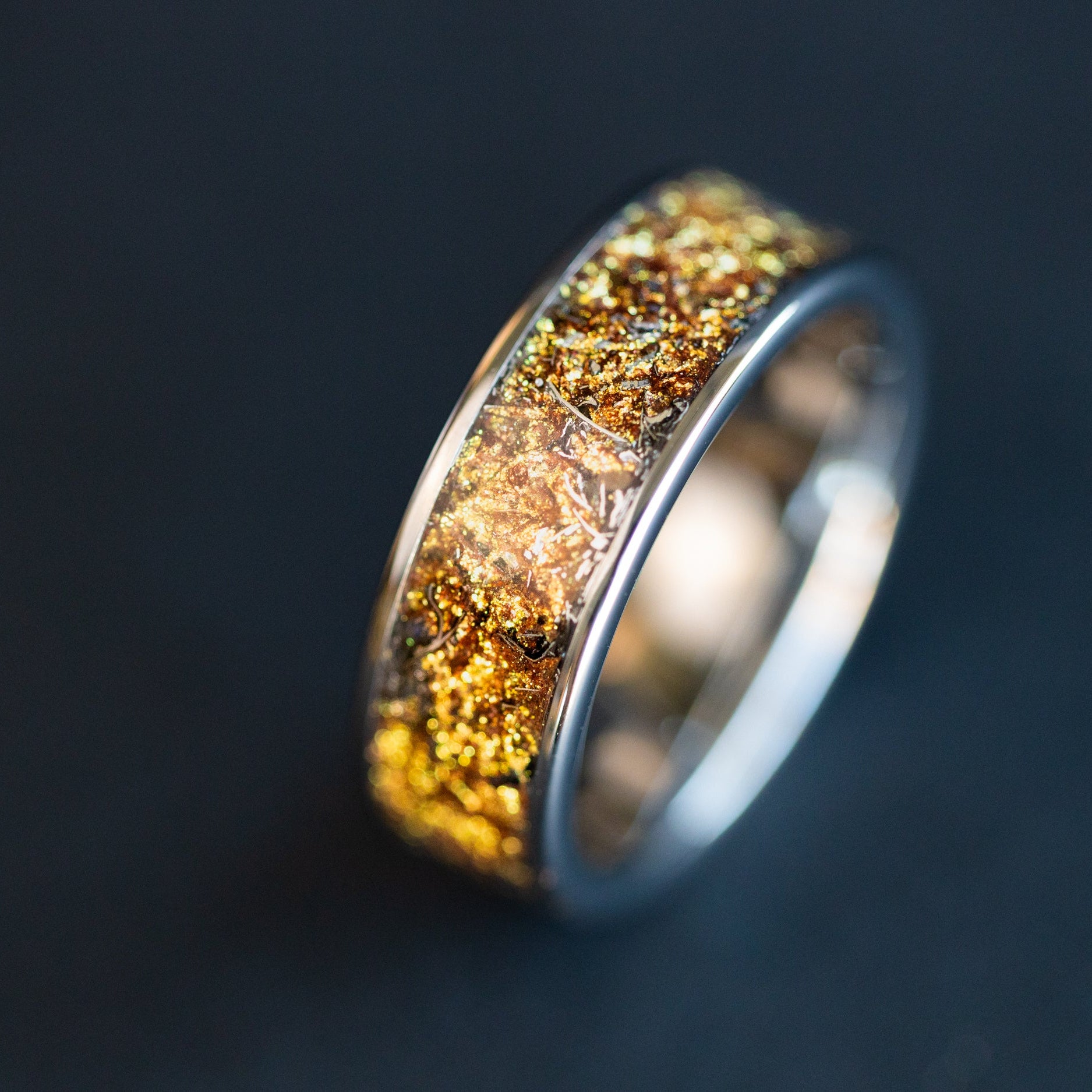 Close up of genuine Campo del Cielo meteorite shavings suspended in warm gold galaxy pigment inlay on 8mm wide channel tungsten ring