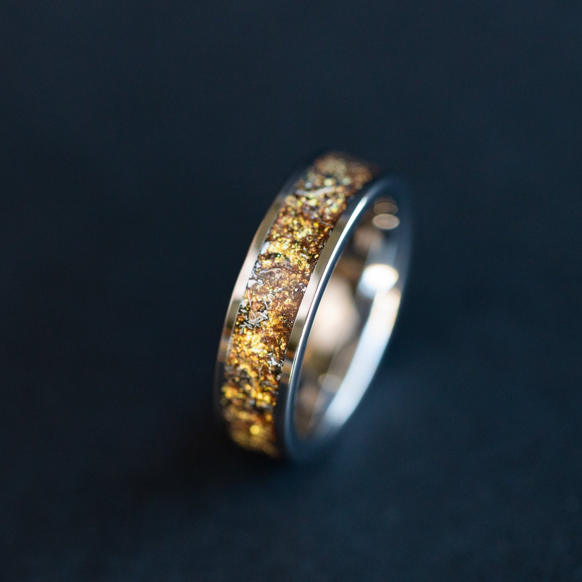 Close up of genuine Campo del Cielo meteorite shavings suspended in warm gold galaxy pigment inlay on 6mm wide channel tungsten ring