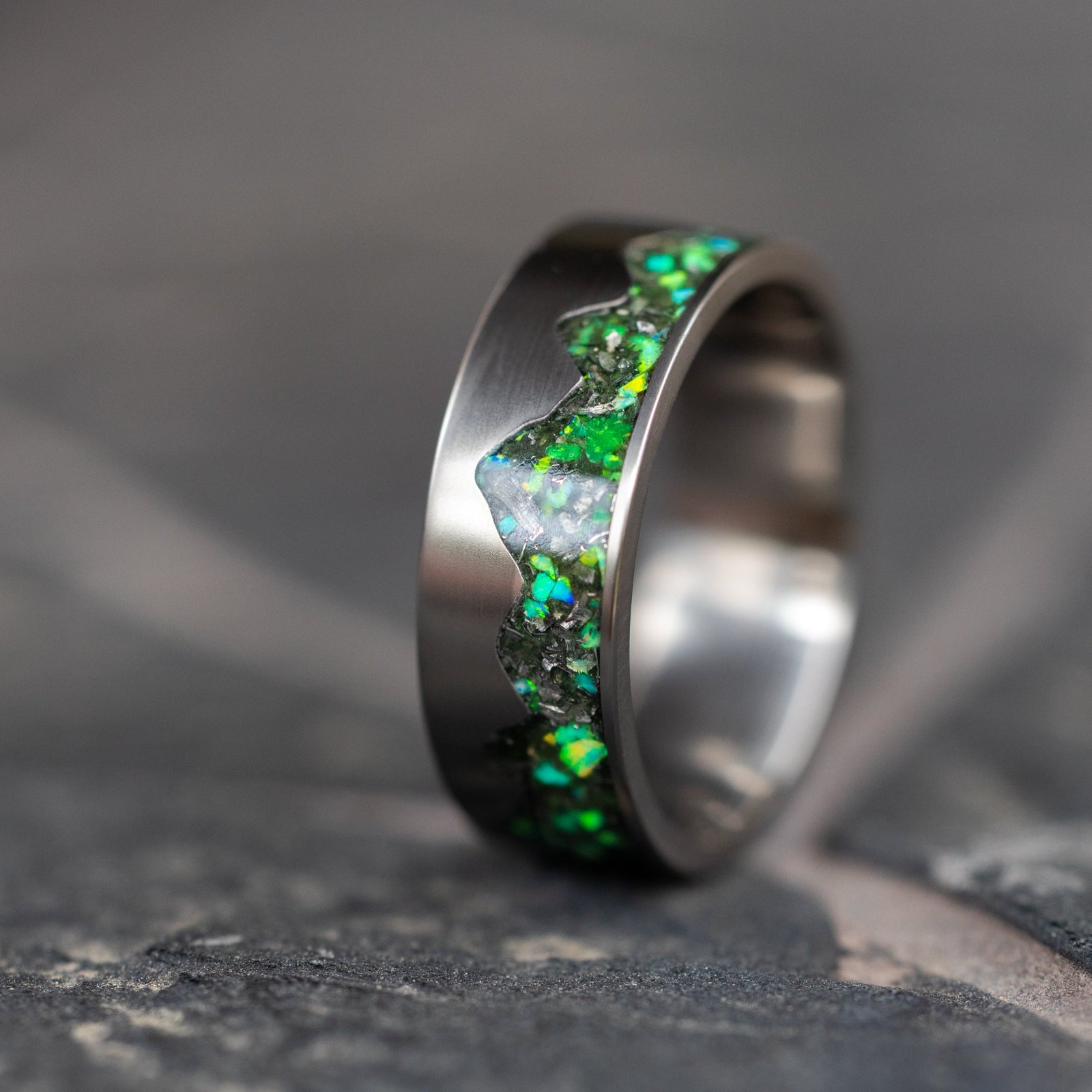 Handcrafted titanium men's wedding band with vibrant green opal and authentic meteorite inlay set in a mountain ridgeline cutout.