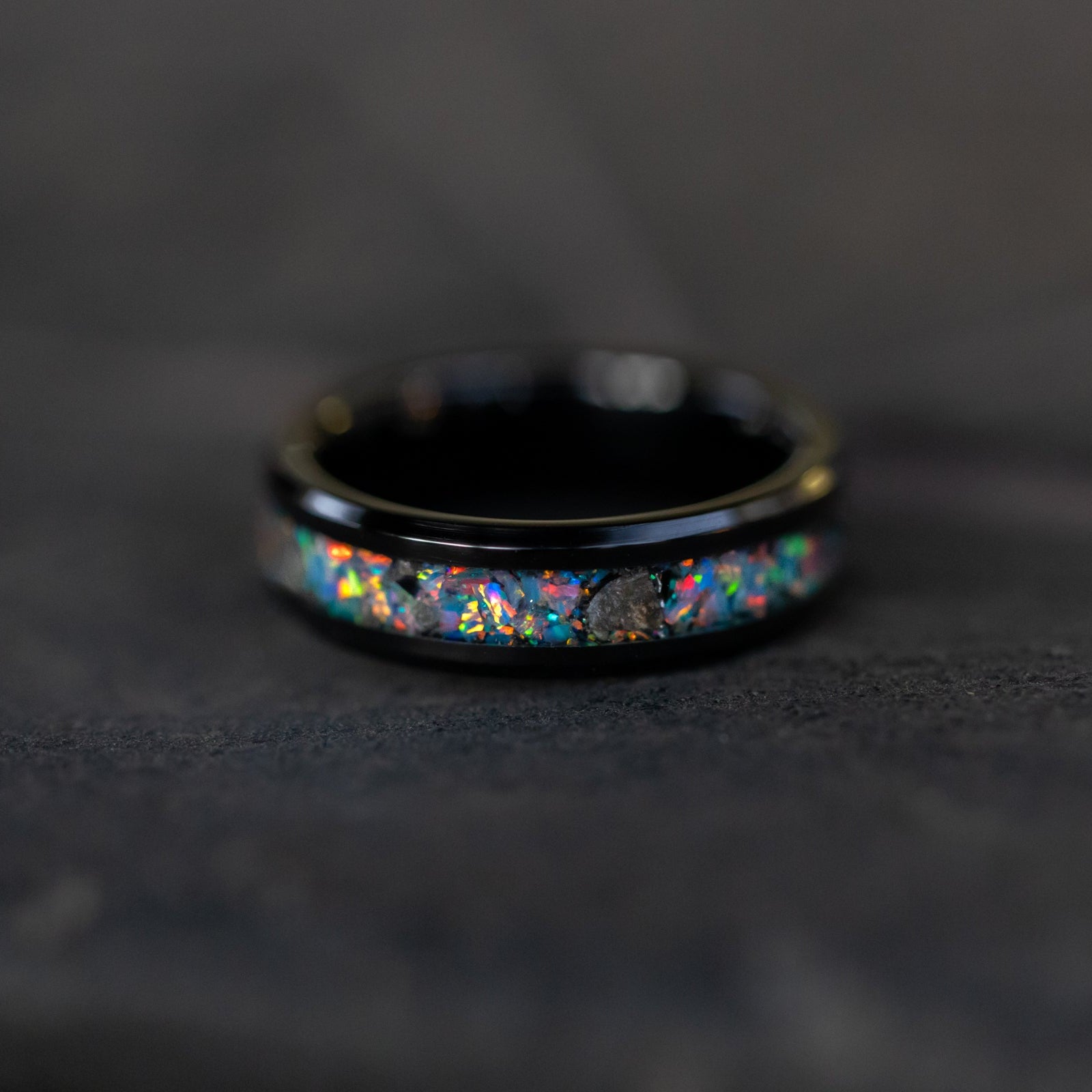Detail shot of the Lunar Relic ring showing authentic lunar meteorite fragments catching light through rainbow moonstone opal inlay on black ceramic band