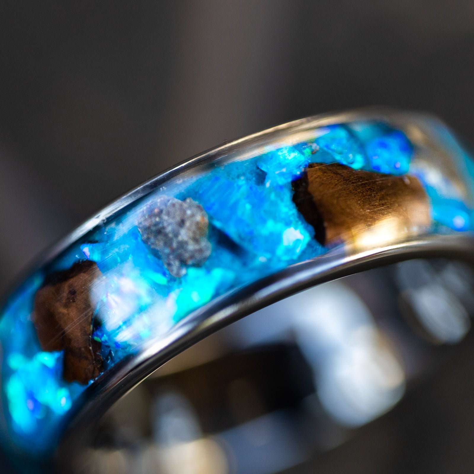 Lunar Rex Glow ring glowing blue in total darkness showing large T-Rex bone pieces and lunar meteorite chunks suspended in electric blue glow in the dark inlay