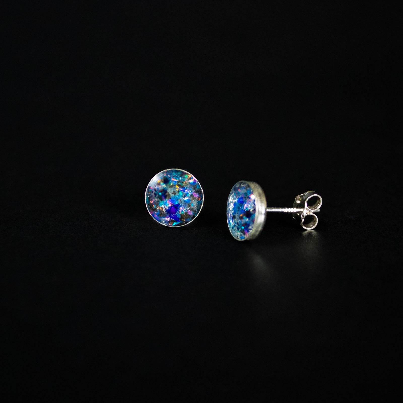 Close-up of the Megalodon Glow Studs shark tooth earrings showing real megalodon tooth, Campo Del Cielo meteorite, and blue and purple opal in each stud
