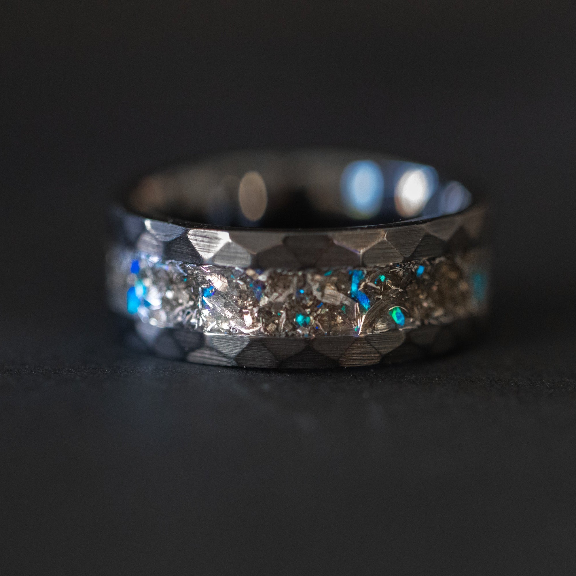 Detail shot of the Meteor Crush ring showing authentic Campo del Cielo meteorite shavings and scattered blue opal accents catching light in hammered black ceramic band