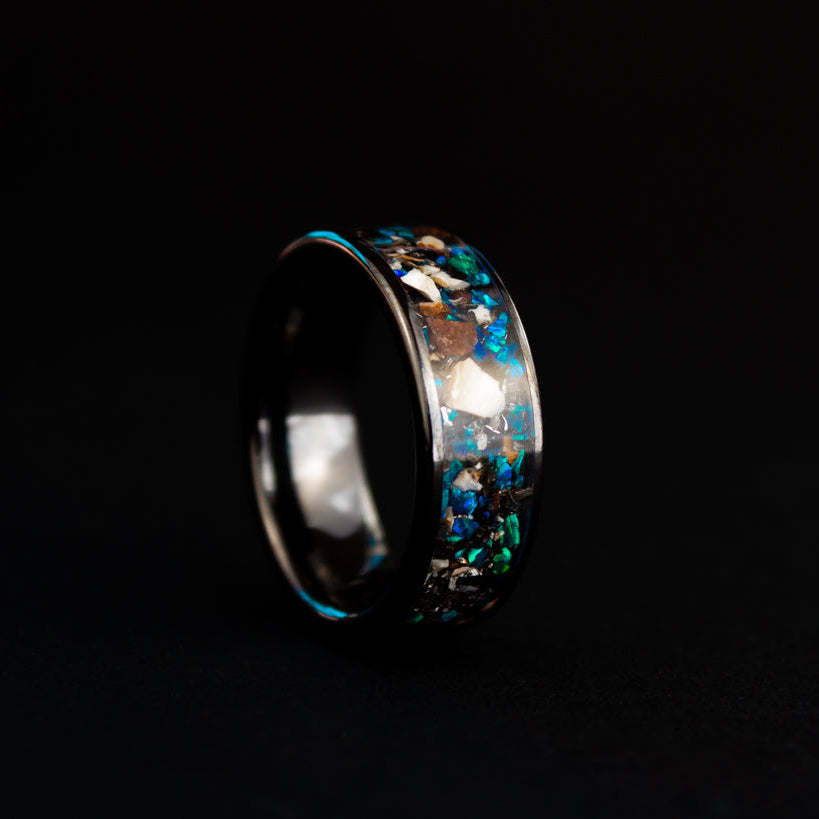 Close up of genuine Mosasaur bone, Dinosaur Gembone, and Campo del Cielo meteorite shavings suspended in blue opal inlay on wide channel black ceramic ring