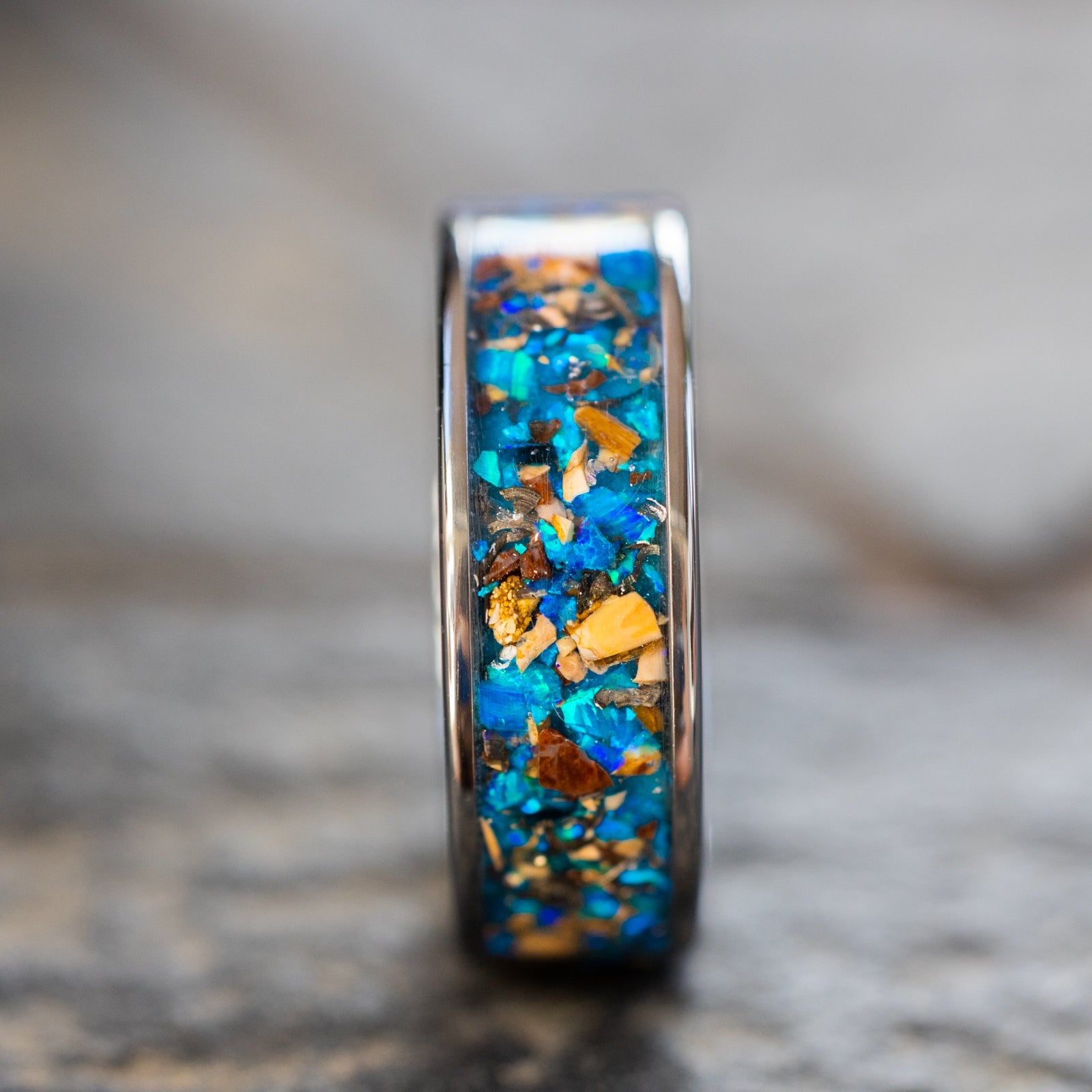 Close up of genuine Mosasaur bone, Dinosaur Gembone, and Campo del Cielo meteorite shavings suspended in blue opal inlay on wide channel tungsten ring