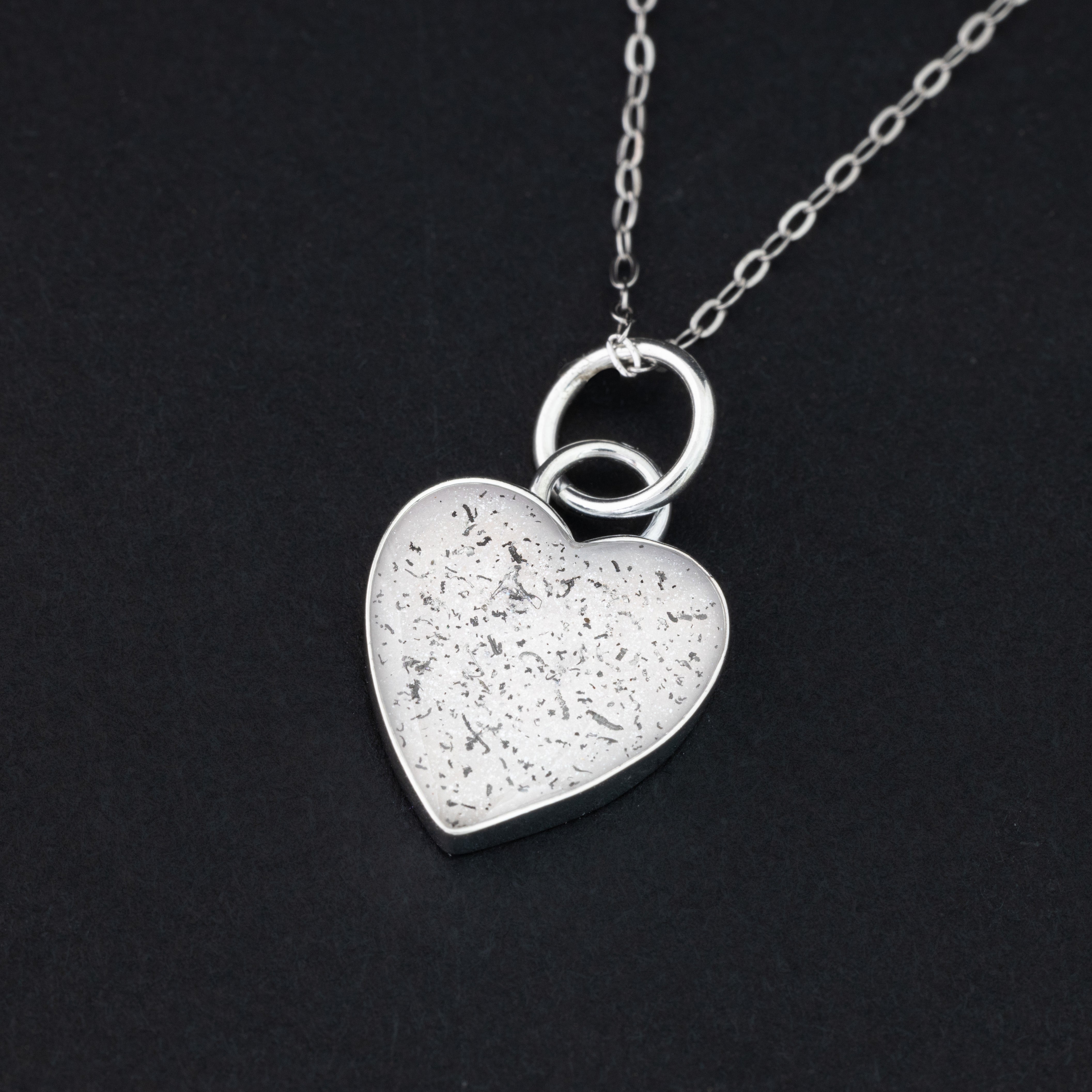 Close-up of the Polar Pulse white heart necklace showing Campo Del Cielo iron meteorite fragments set in clean white resin
