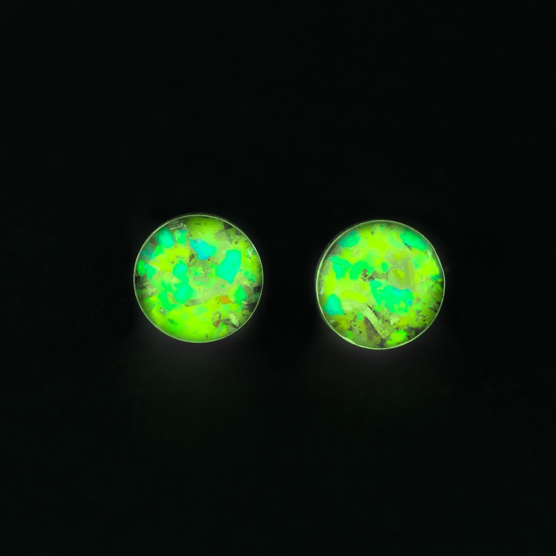 Close-up of the Radioactive Velociraptor Studs glow in the dark earrings showing Campo Del Cielo iron meteorite, real velociraptor bone, and vivid green opal in sterling silver