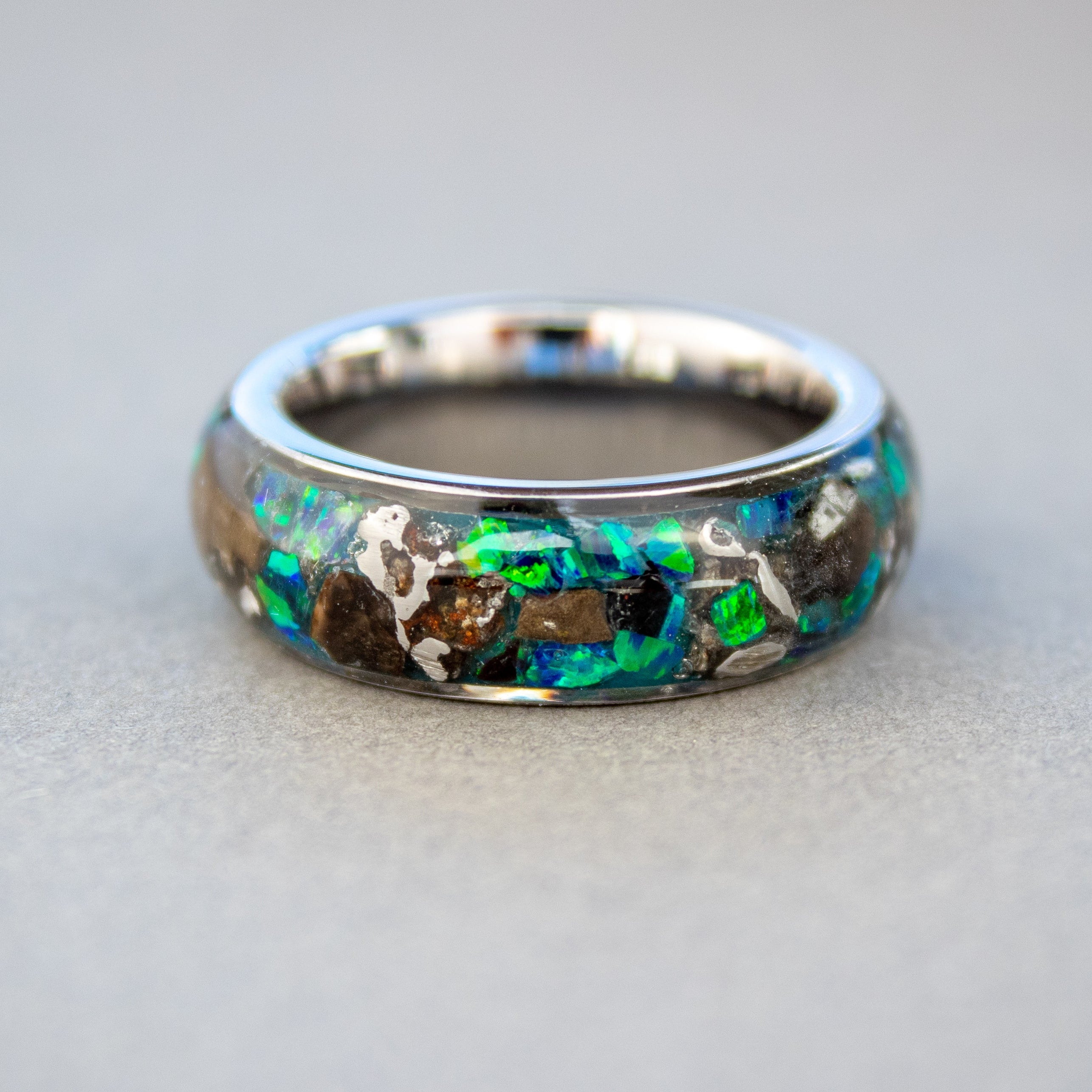 Rex Relic ring glowing blue in total darkness showing large T-Rex bone pieces and meteorite chunks suspended in electric blue glow in the dark inlay