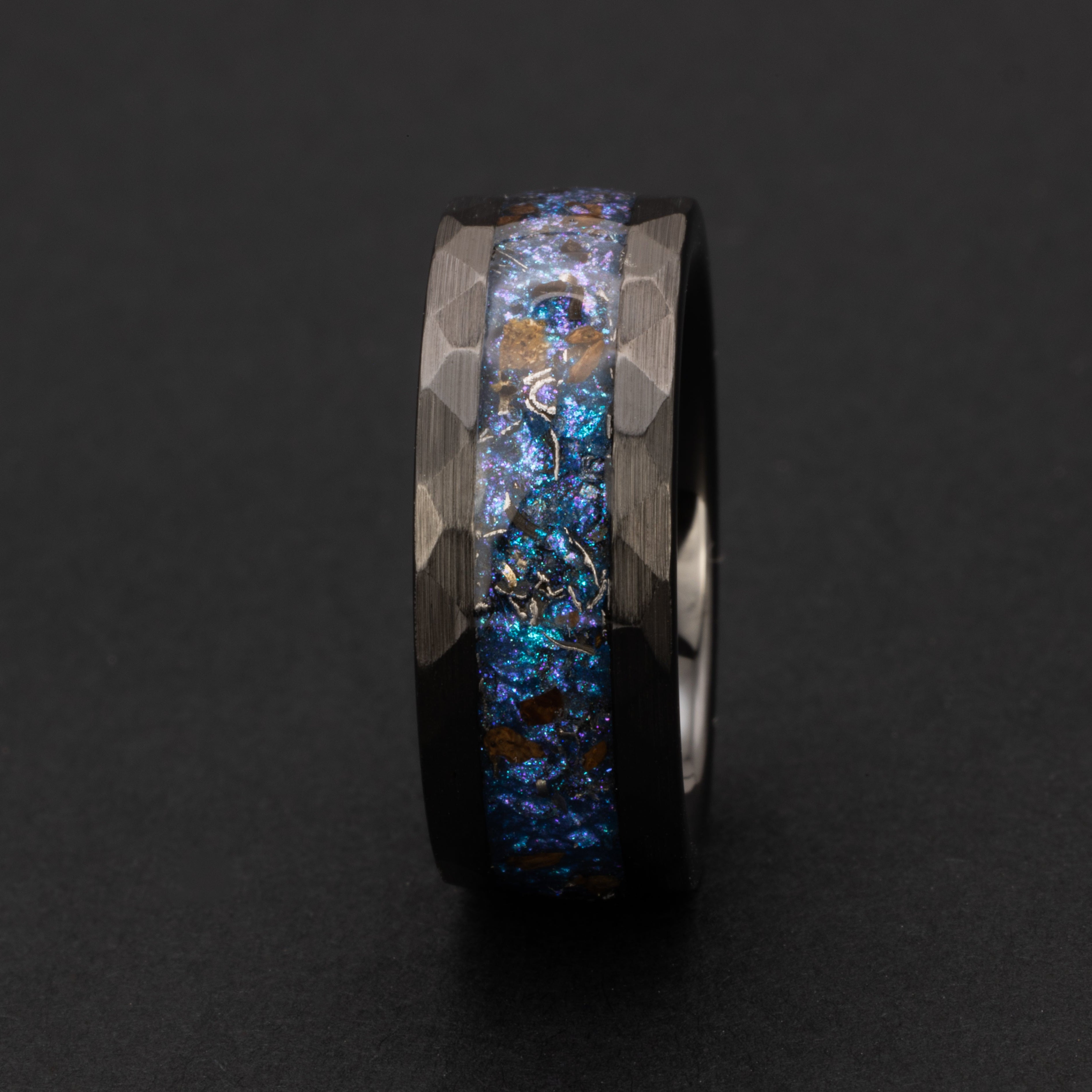 Close up of genuine T-Rex fossil and Campo del Cielo meteorite shavings suspended in blue and purple opal galaxy glitter inlay on hammered black ceramic ring