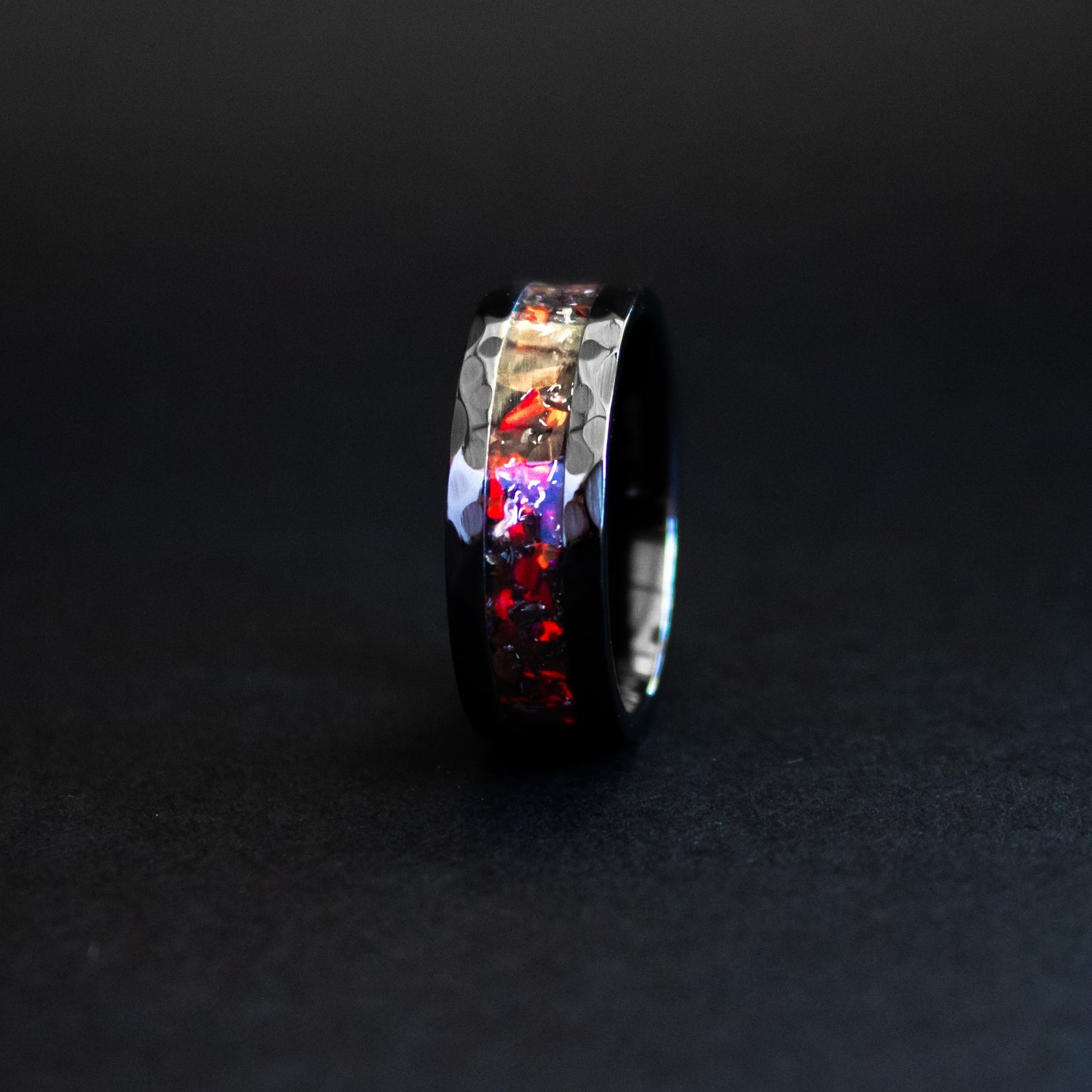 Close up of genuine T-Rex fossil and Campo del Cielo meteorite shavings suspended in red opal inlay on hammered black ceramic ring