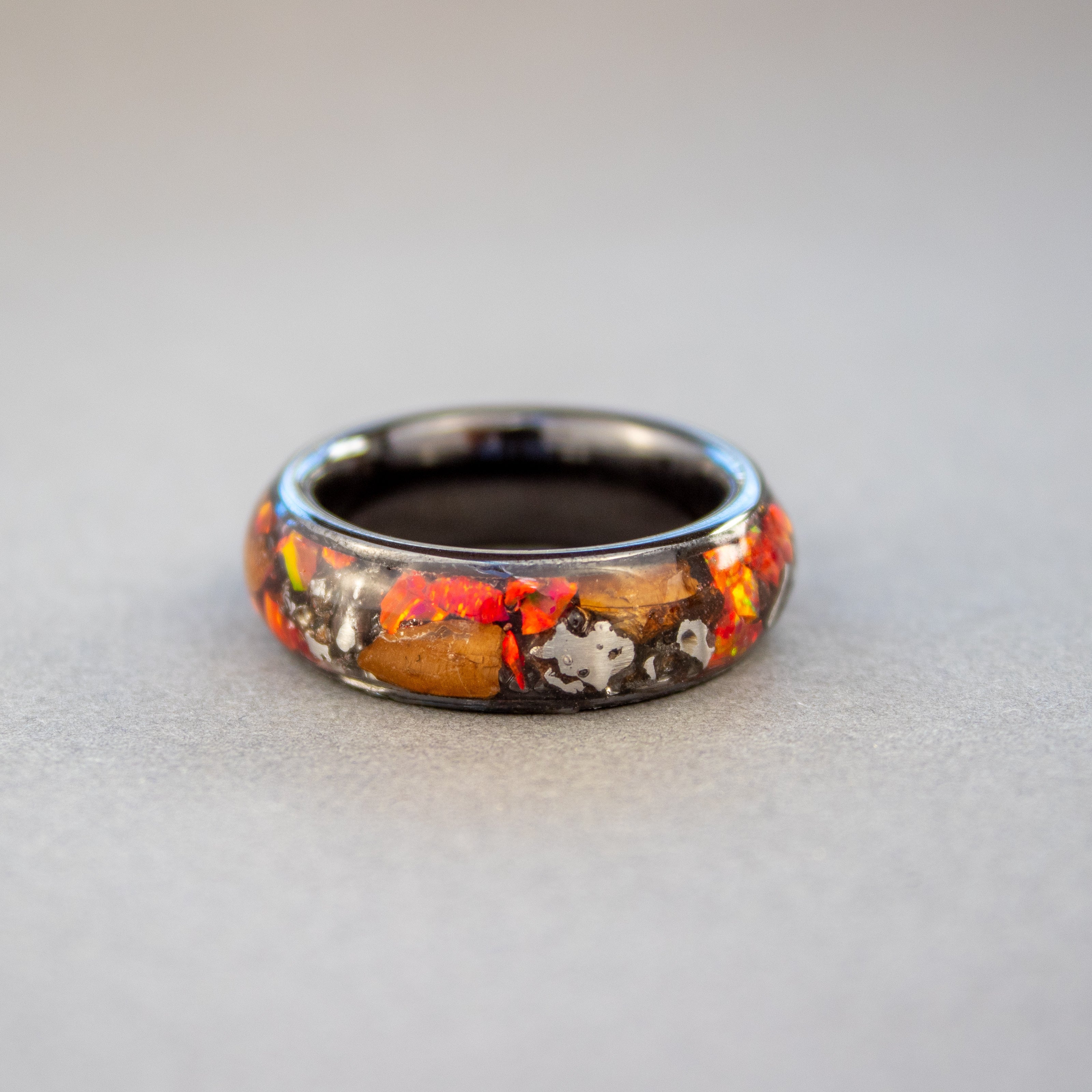 Close up of large genuine Triceratops fossil pieces and Campo del Cielo meteorite chunks surrounded by red opal inlay on wide channel black ceramic ring