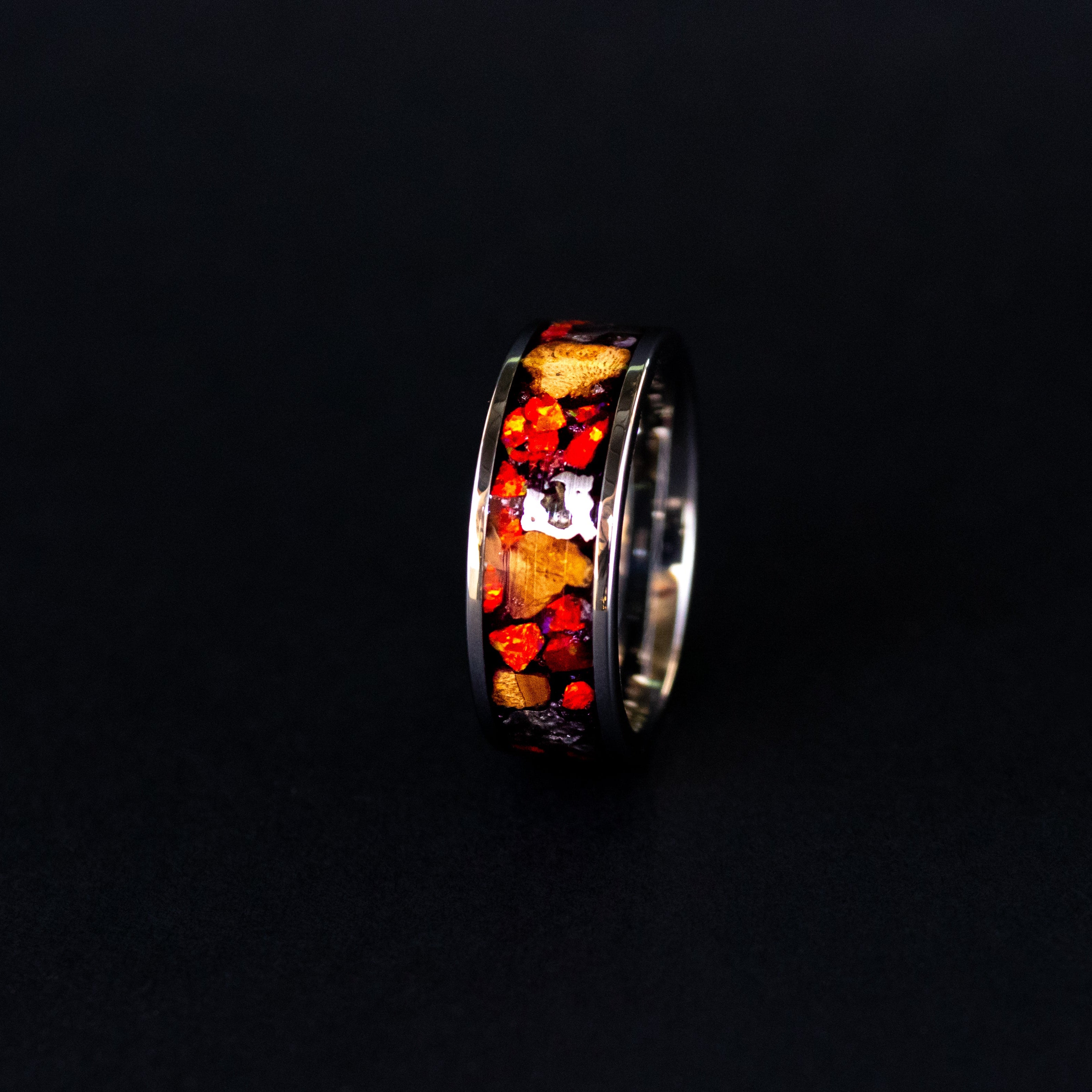 Close up of large genuine Triceratops fossil pieces and Campo del Cielo meteorite chunks surrounded by red opal inlay on wide channel tungsten ring