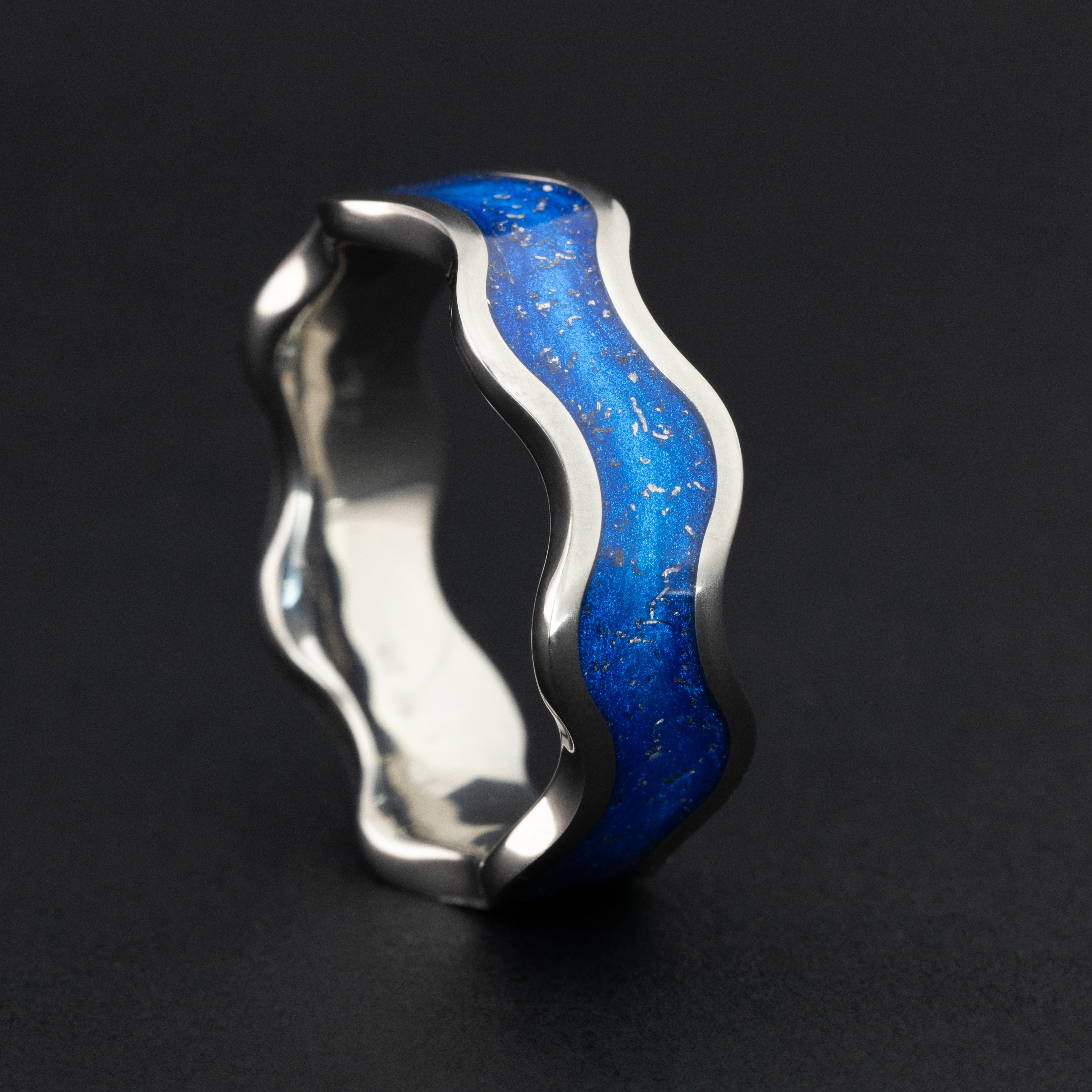 Close up of genuine Campo del Cielo meteorite pieces suspended in blue resin inlay following the wave profile of the titanium wiggle band