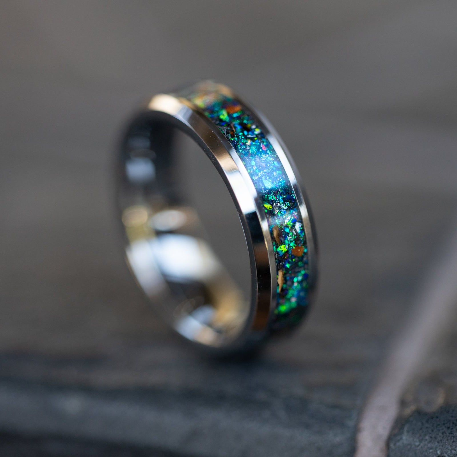 Close up of genuine Velociraptor fossil and Campo del Cielo meteorite shavings suspended in blue green and purple opal galaxy inlay on beveled tungsten ring