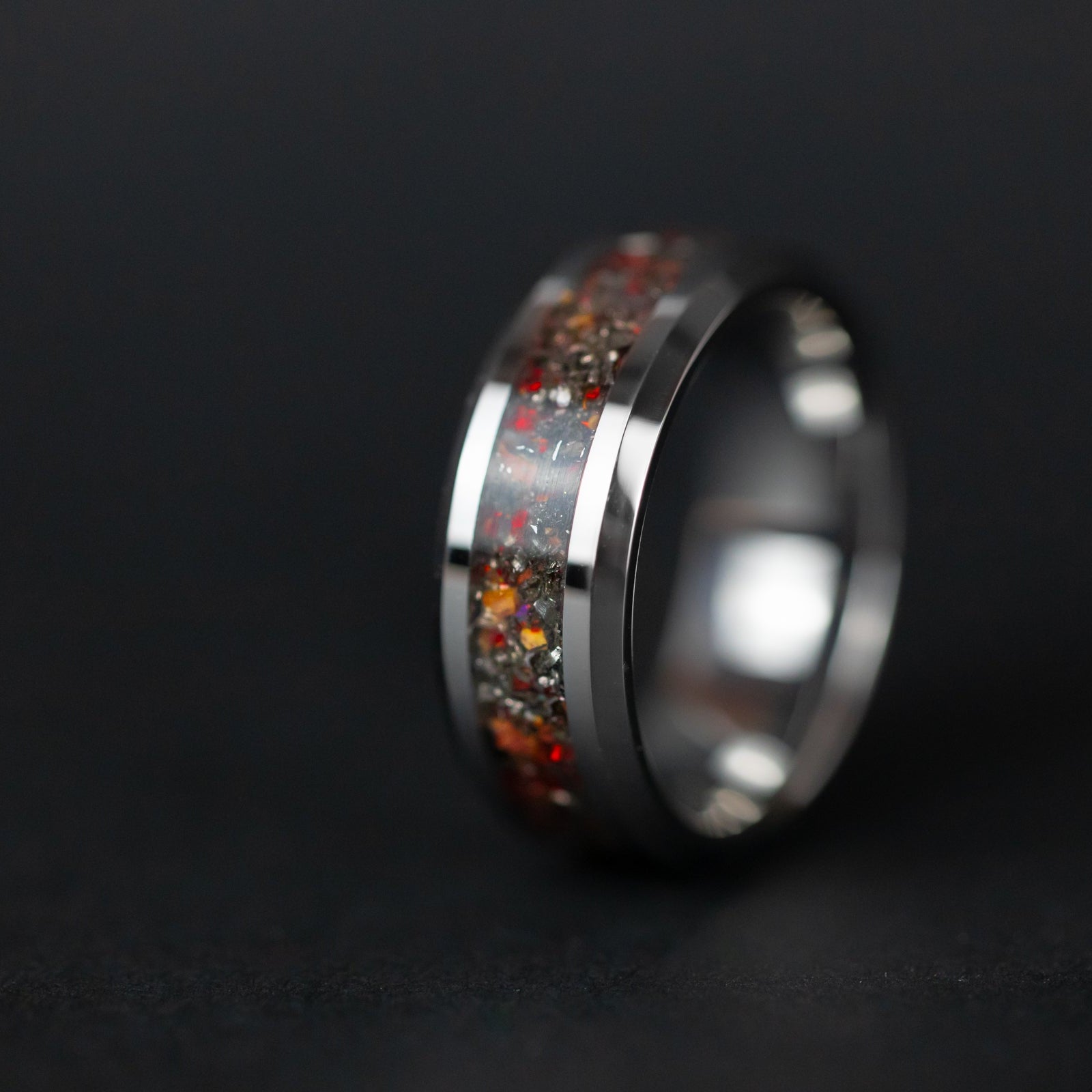 Close up of genuine Velociraptor fossil and Campo del Cielo meteorite shavings with scattered red opal accents on beveled tungsten ring