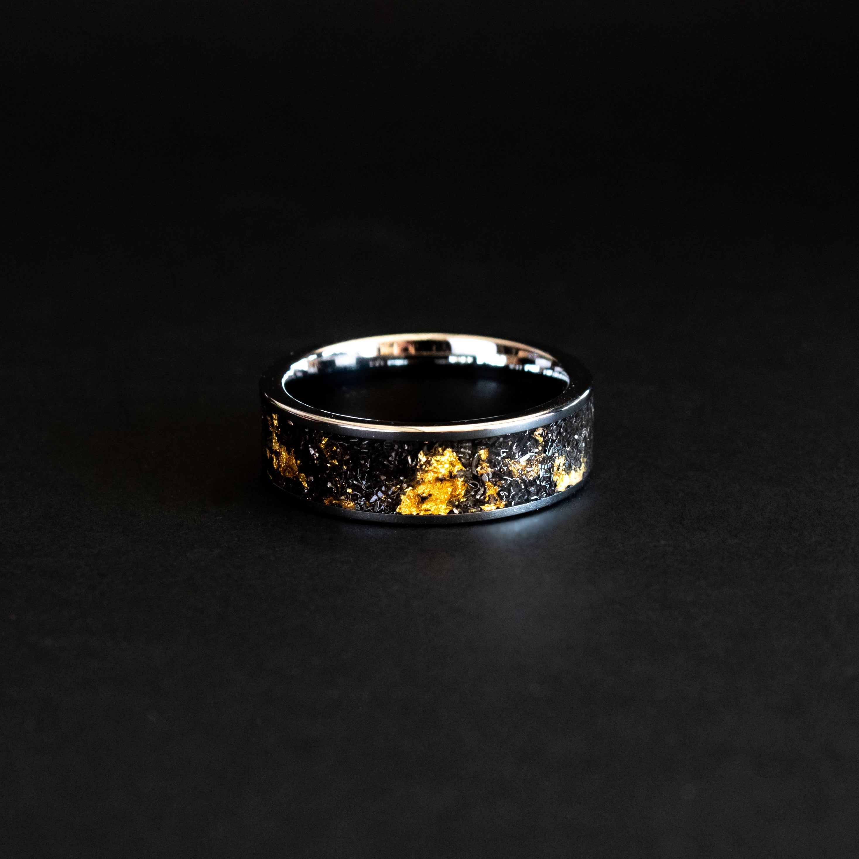Detail shot of the 24K Cosmic Gold ring showing authentic Campo del Cielo meteorite shavings and real gold metal flake catching light on wide channel tungsten band