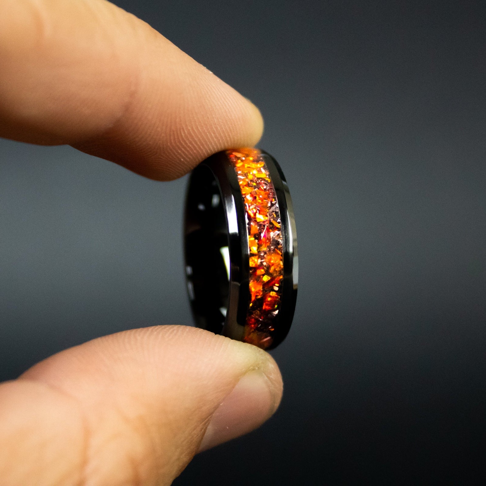 Detail shot of the Amber Cosmos ring showing authentic Campo del Cielo meteorite shavings catching light through bright orange opal inlay on black ceramic band