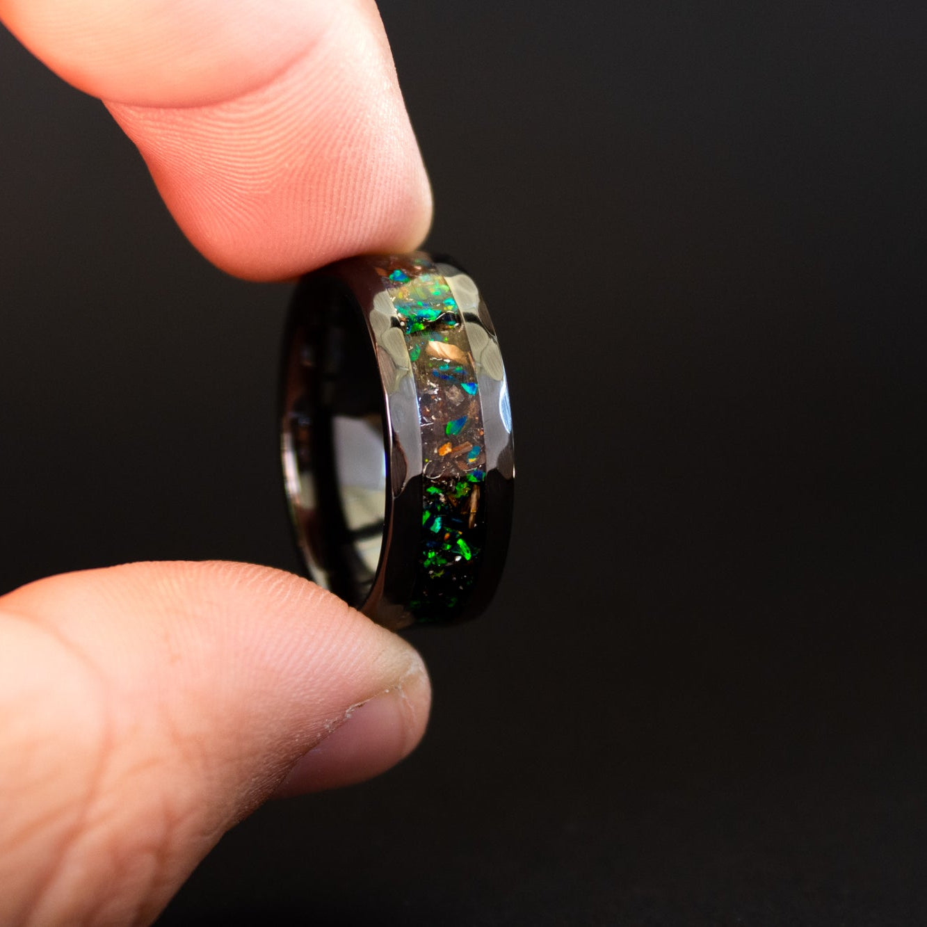 Detail shot of the Apex Green ring showing authentic T-Rex bone fragments and meteorite shavings catching light through green opal inlay on hammered black ceramic band