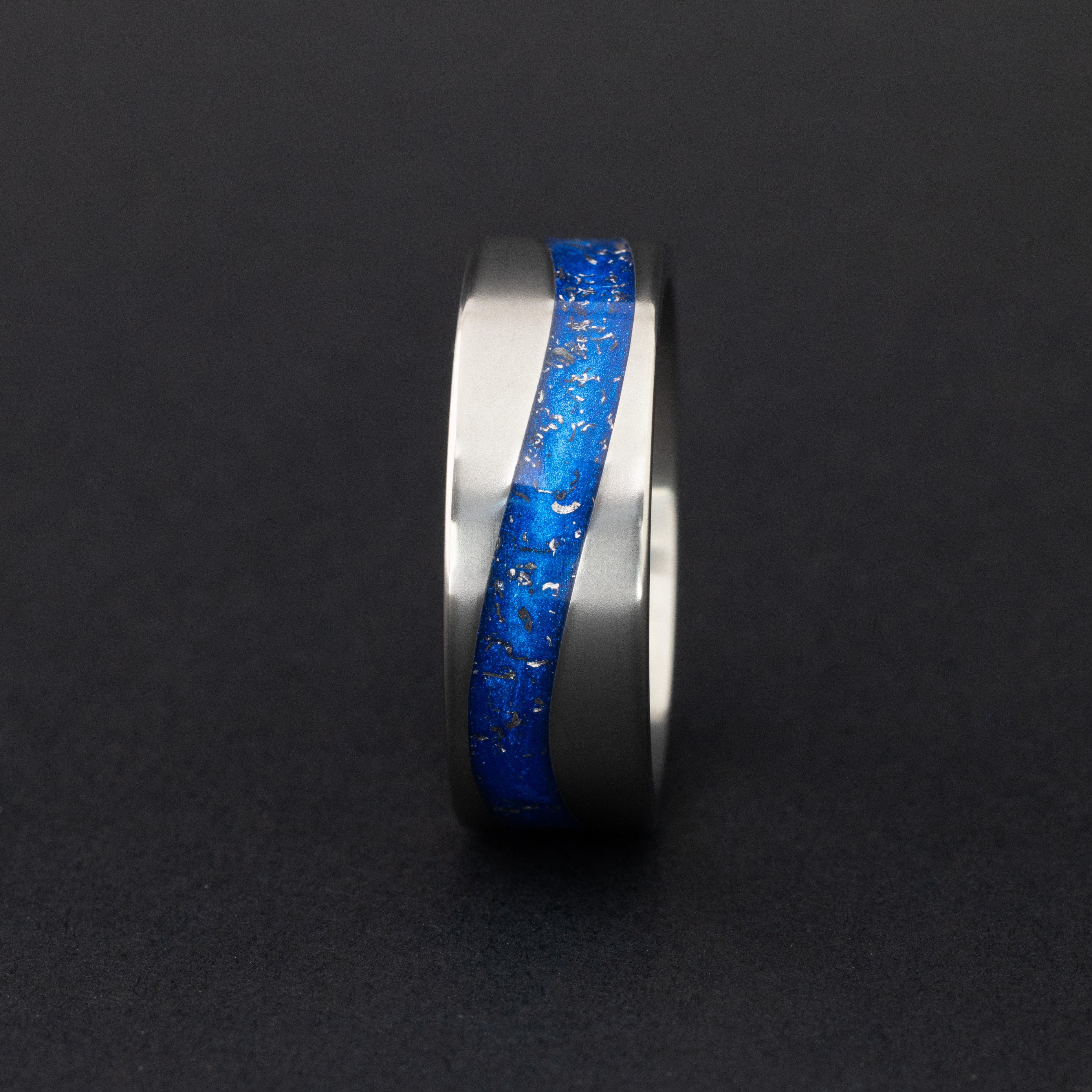 Detail shot of the Blue Drift ring showing authentic Campo del Cielo meteorite pieces drifting through blue resin in curved inlay channel on tungsten band
