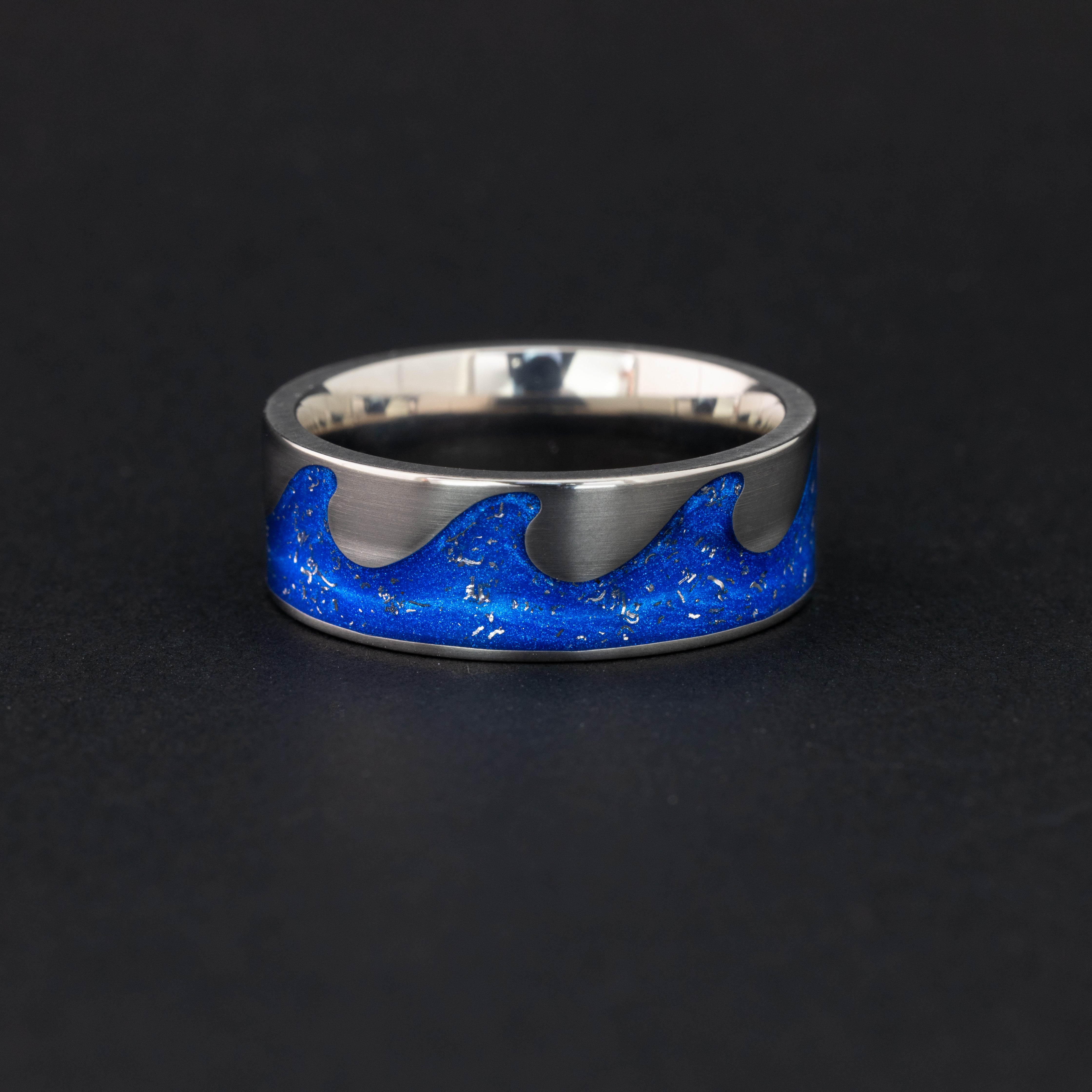 Detail shot of the Blue Orbit Riptide ring showing authentic Campo del Cielo meteorite pieces drifting through blue resin in the wave-shaped titanium riptide channel