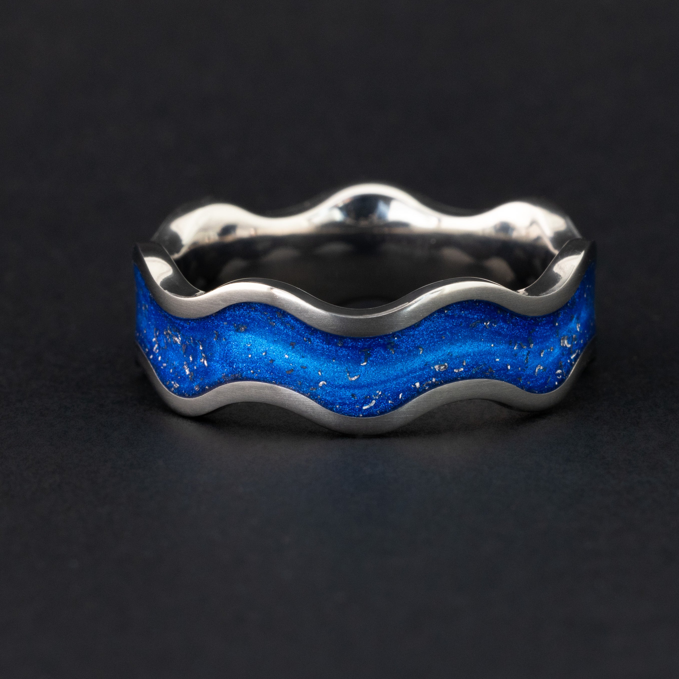 Detail shot of the Blue Orbit Wiggle ring showing authentic Campo del Cielo meteorite pieces drifting through blue resin inlay on titanium wiggle band with wave profile